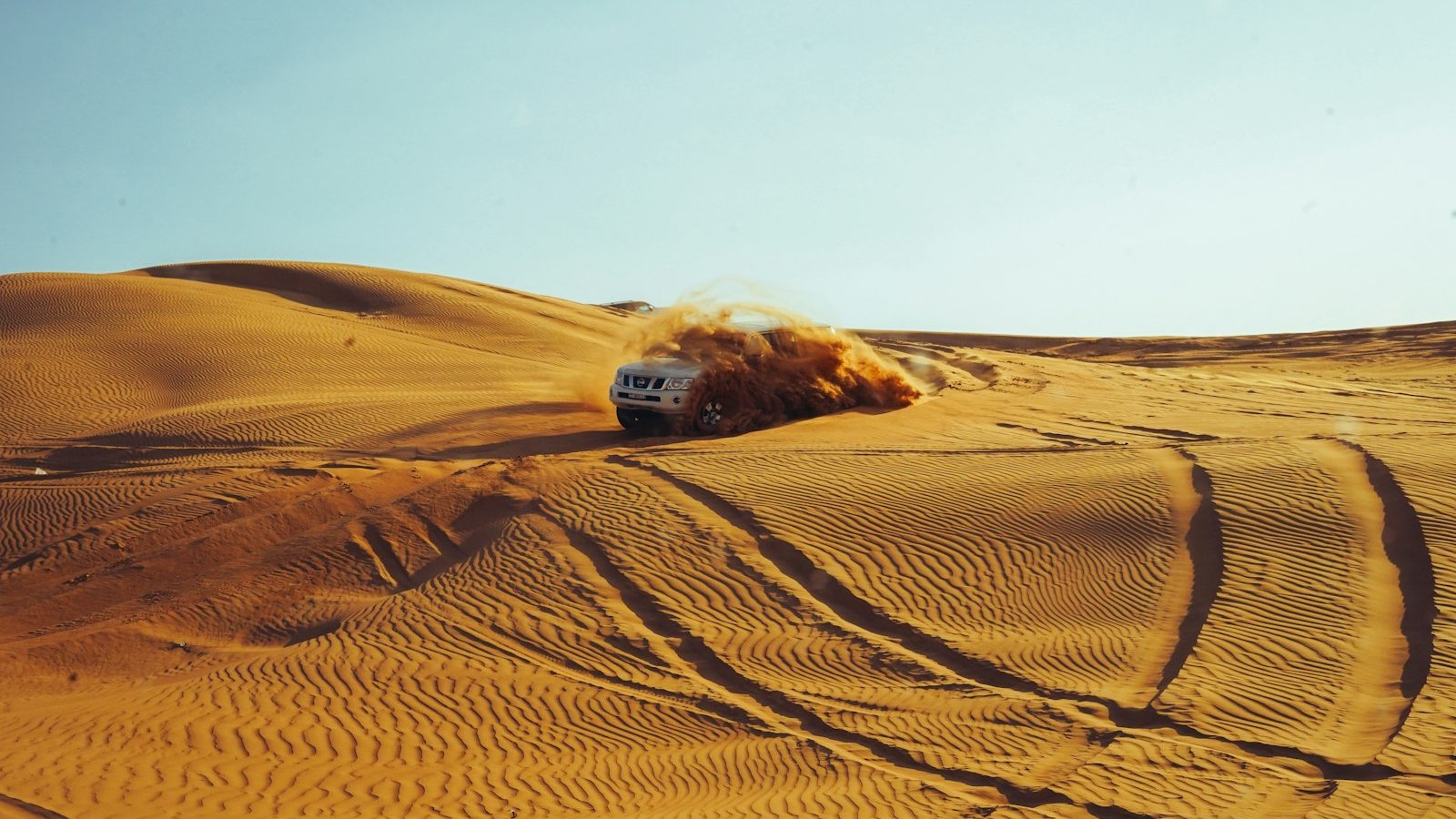 A 4x4 carving down a sand dune throwing up a plume of sand