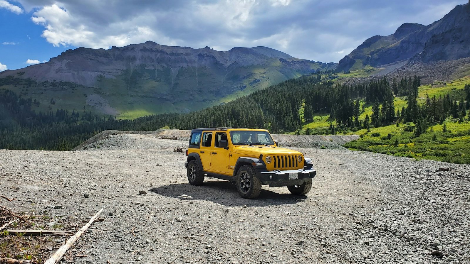 Yellow Jeep Wrangler parked on a trail in a green alpine valley