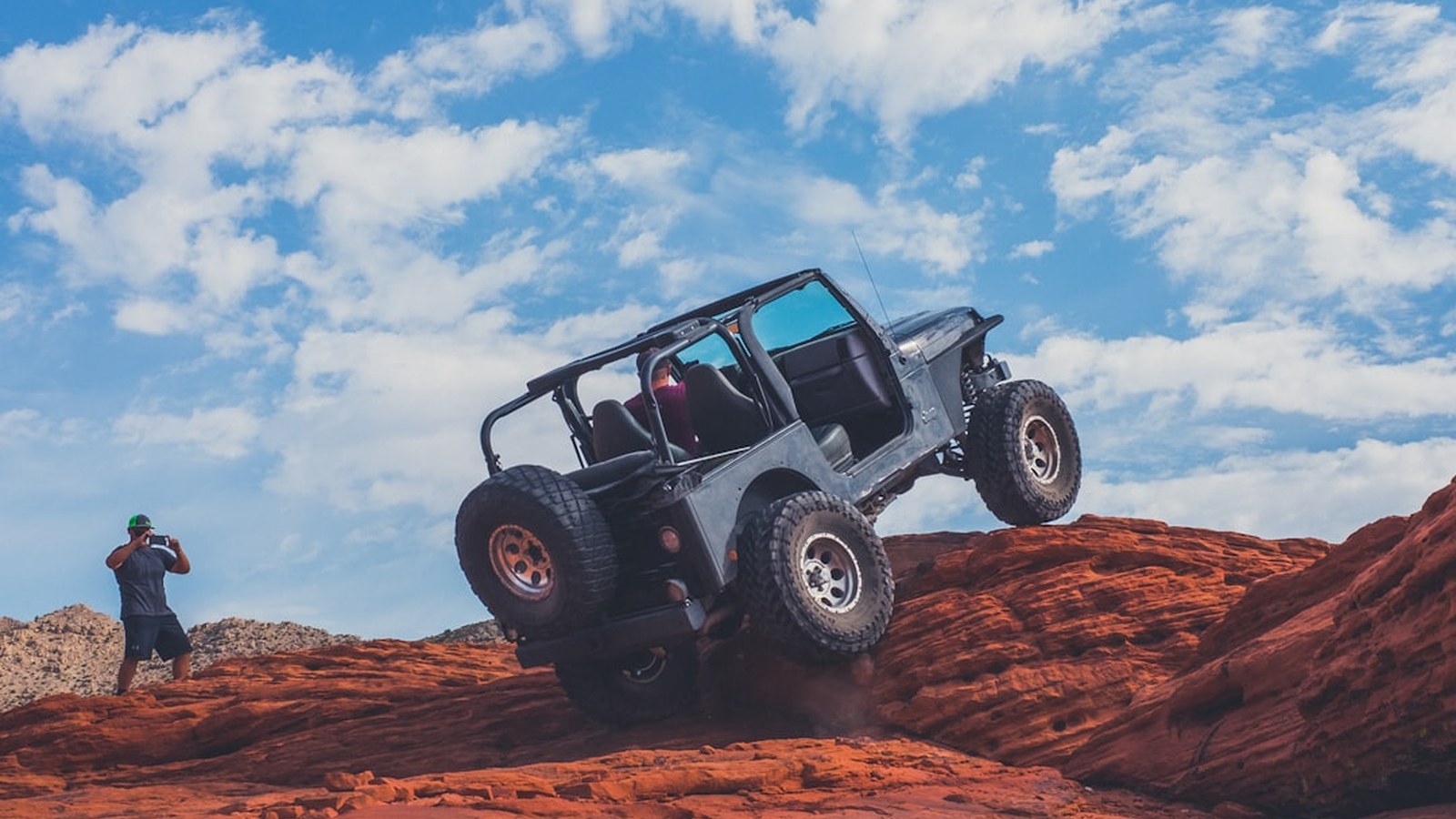 A Jeep articulated nose-down on a steep red rock ledge, a hard obstacle above a beginner's skill level
