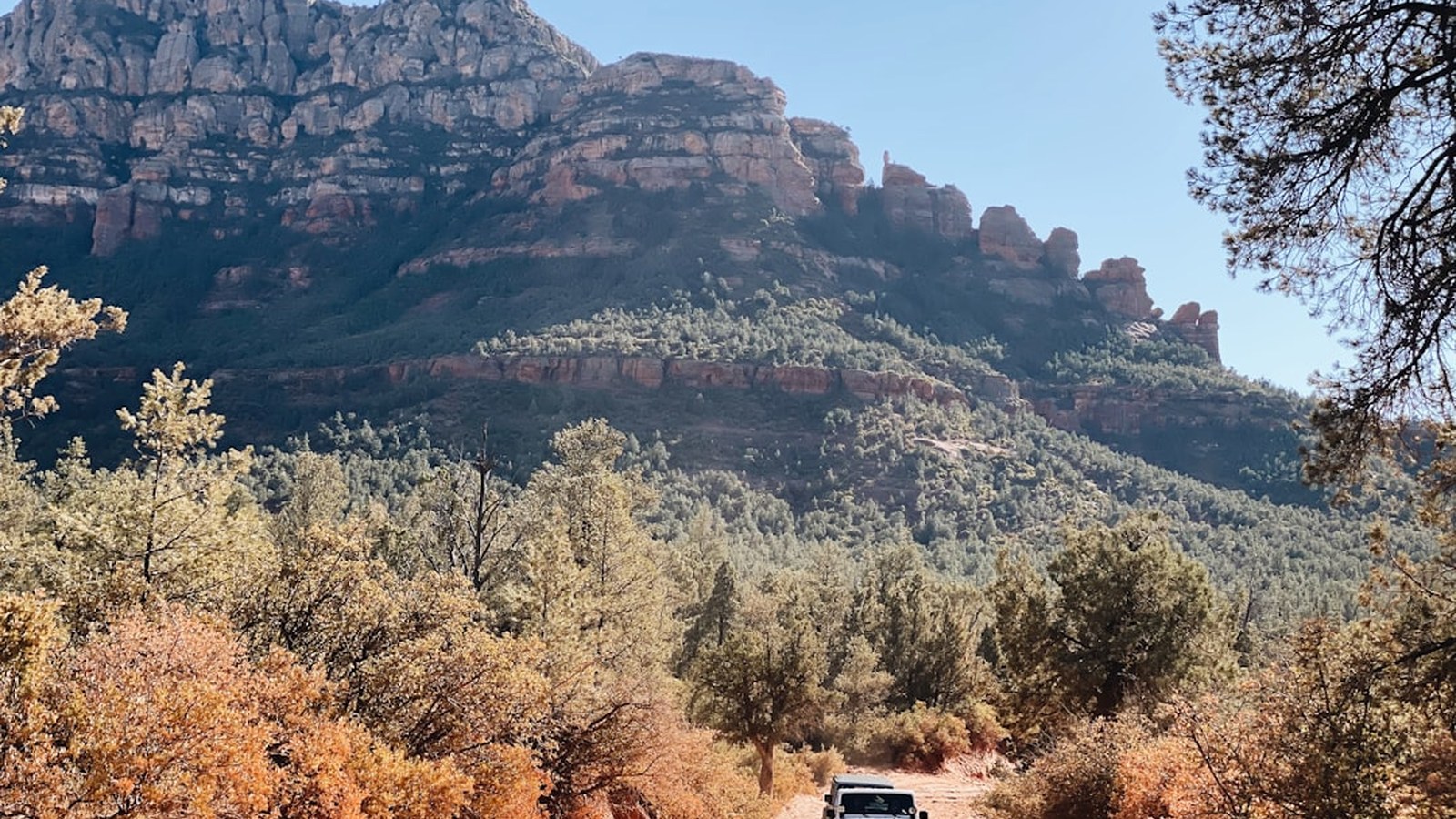 An off-road rig on a designated dirt trail with a dramatic red-rock backdrop, staying on route to protect access