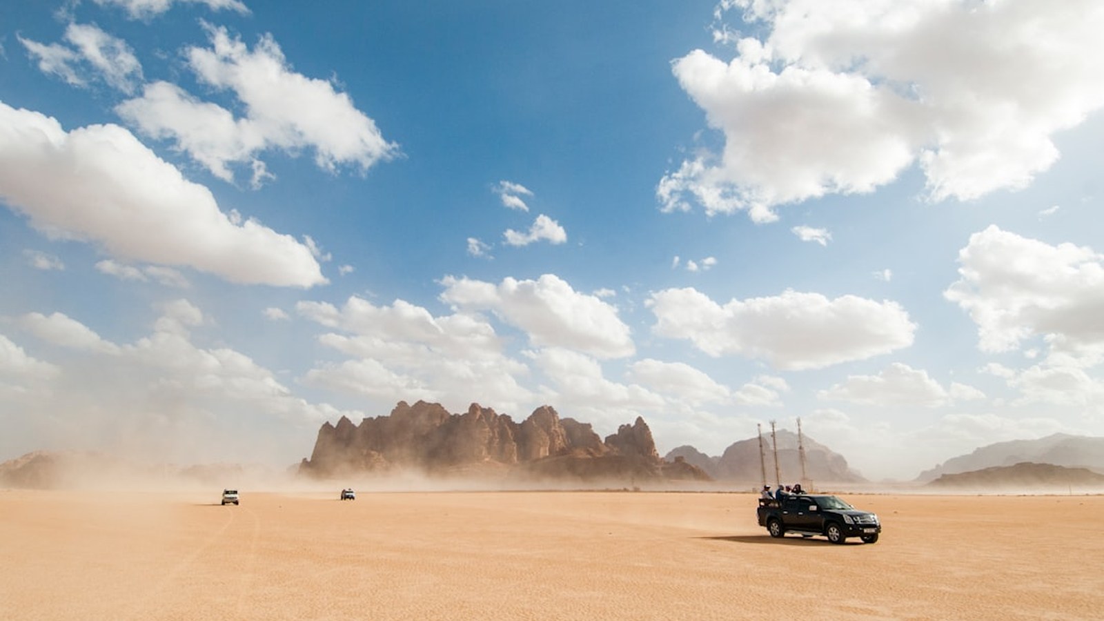 A convoy of rigs crossing open desert with dust and rock spires under a big sky, the payoff of a well-planned trip