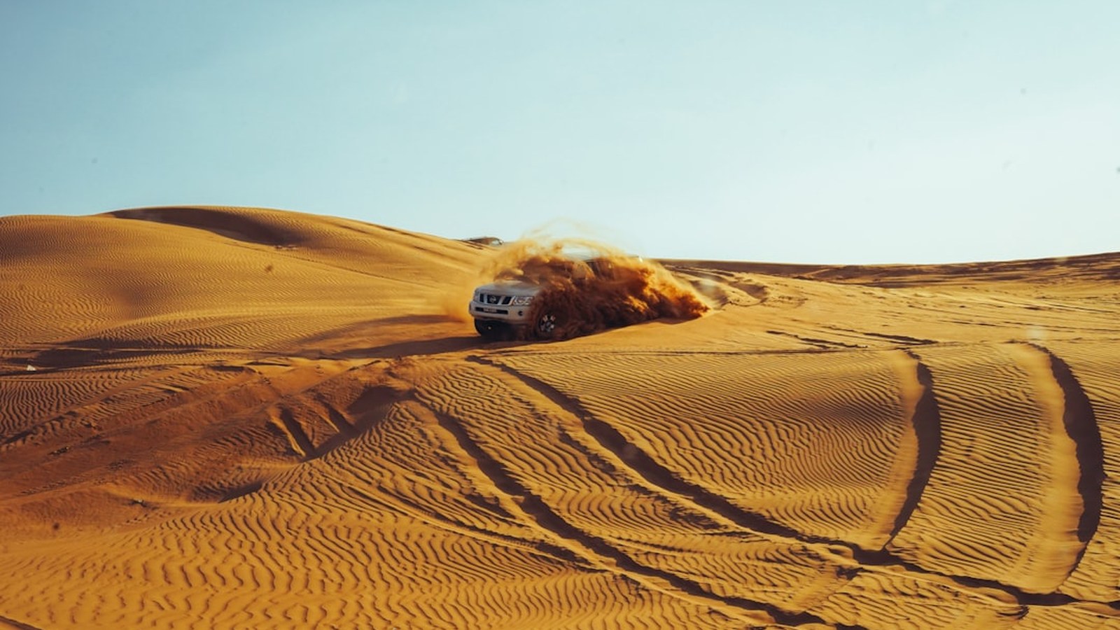An SUV kicking up a golden dust plume on a sand dune, where smooth throttle control matters most