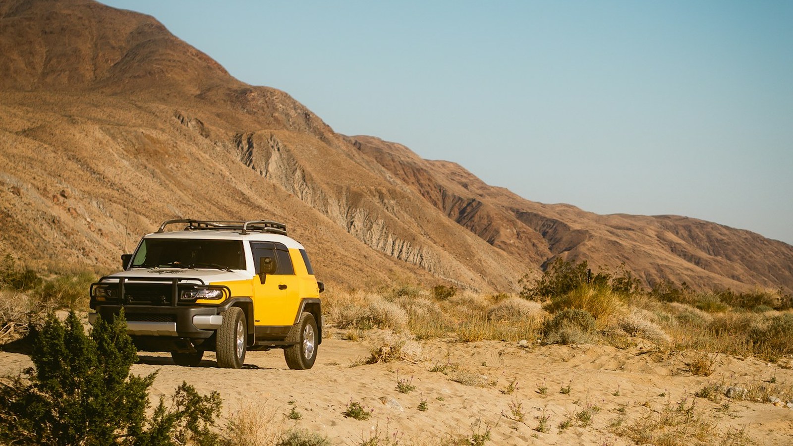 FJ Cruiser driving through a sandy desert wash with a mountain backdrop