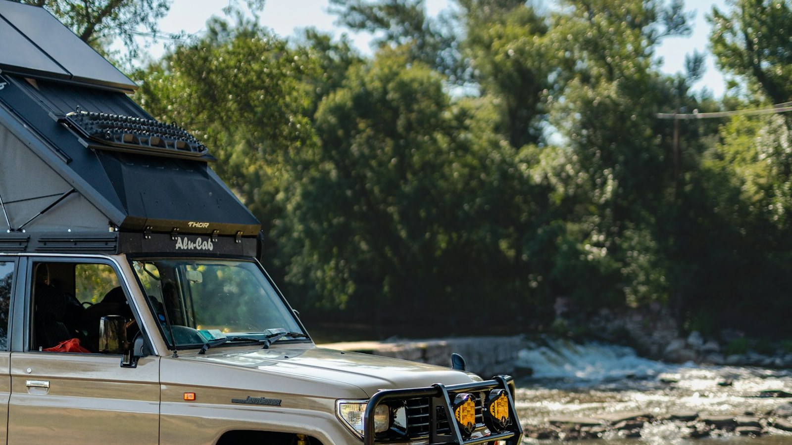 Kitted Land Cruiser camped beside a river in a green valley at golden hour