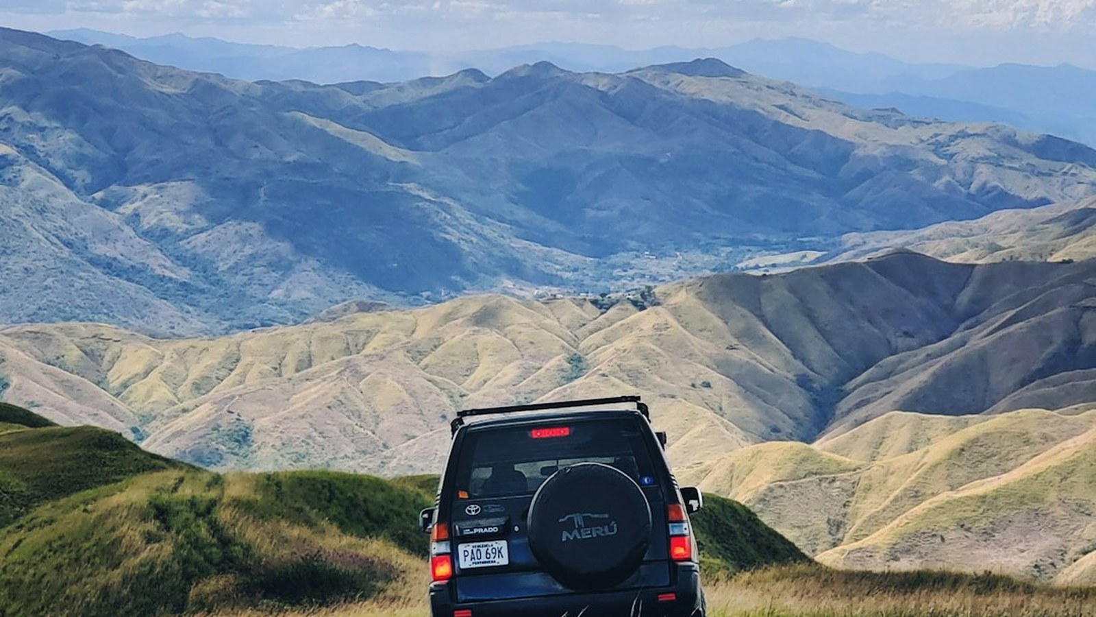 SUV driving a grassy two-track toward distant mountains