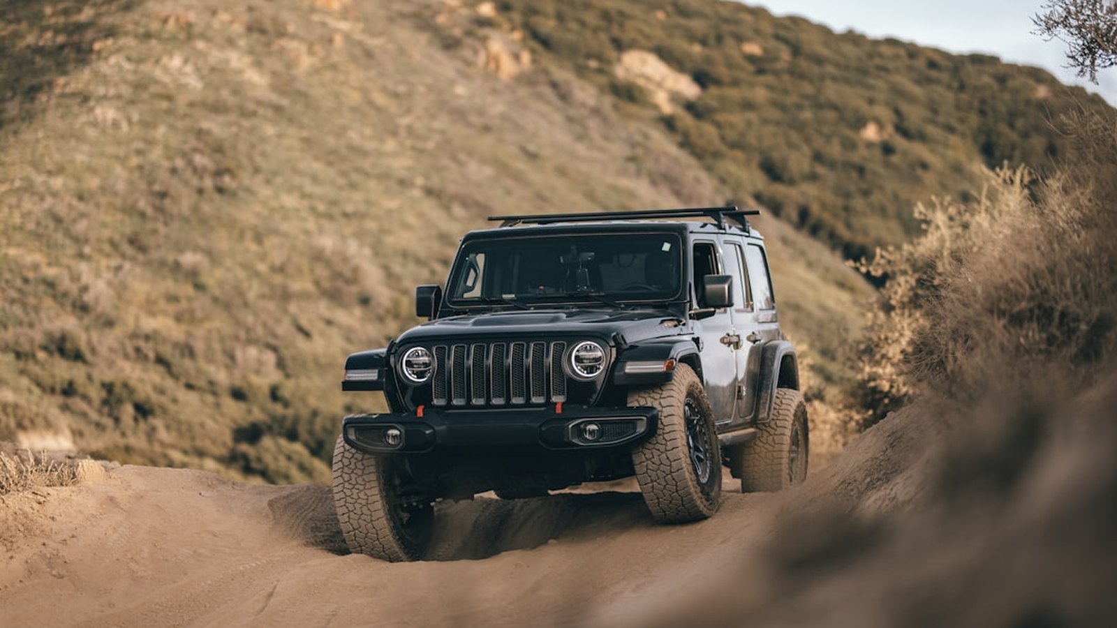 Lifted Jeep Wrangler kicking up dust on a mountain trail