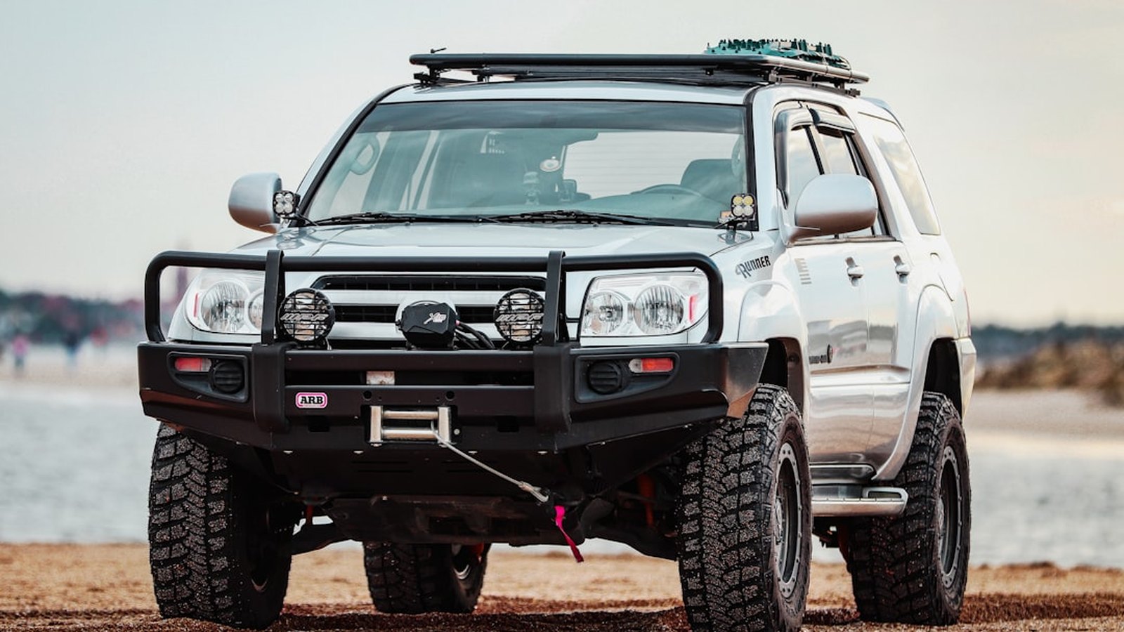 Built 4Runner with a bull bar, winch, aux lights and roof rack parked on dirt
