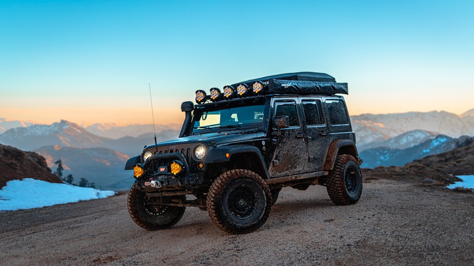 Kitted overland Jeep Wrangler with a light bar on a mountain ridge at blue hour