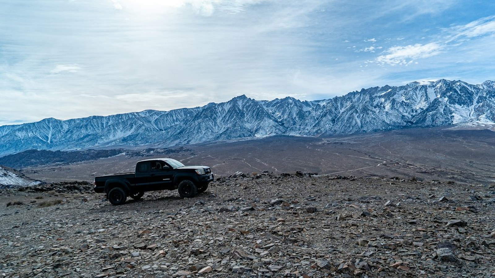 A lone overland truck dwarfed by a snow-capped Sierra mountain range in a wide open vista