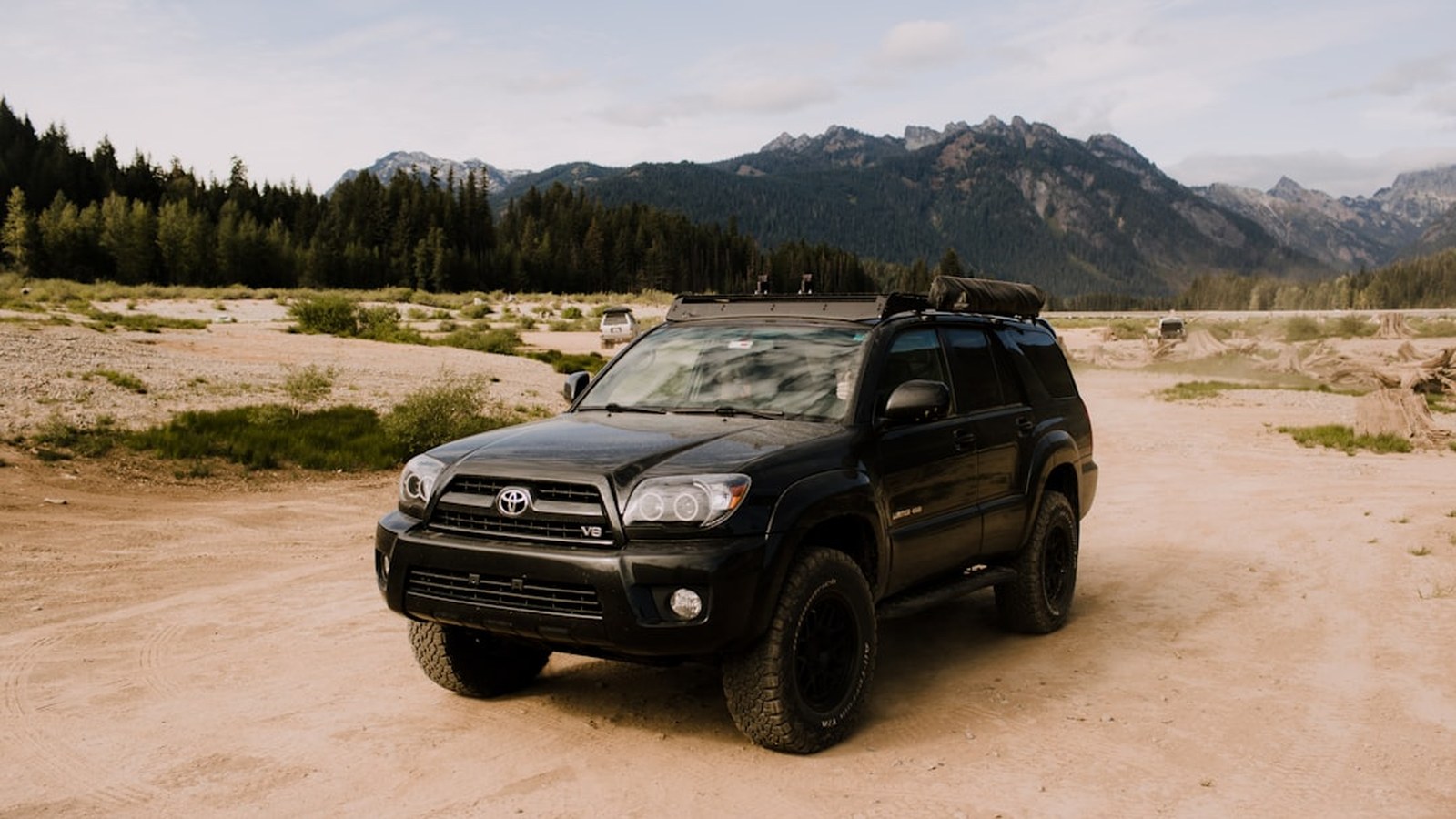 Black Toyota 4Runner on all-terrain tires parked on a dry desert flat below a forested ridge