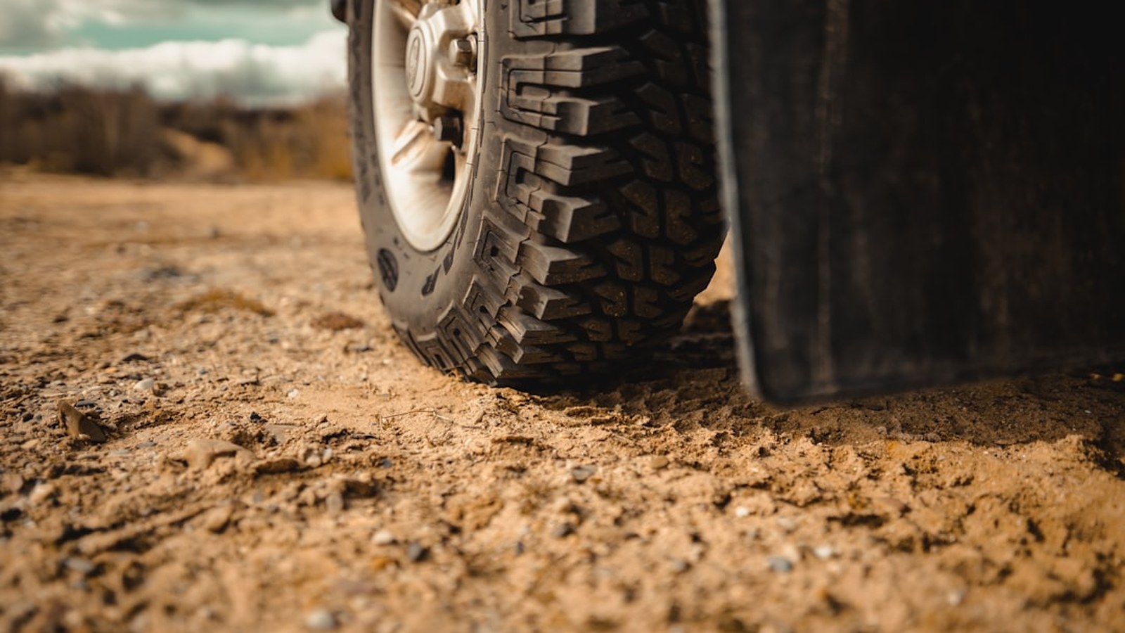Chunky off-road tire on a 4x4 parked on a gravel trail under a moody sky