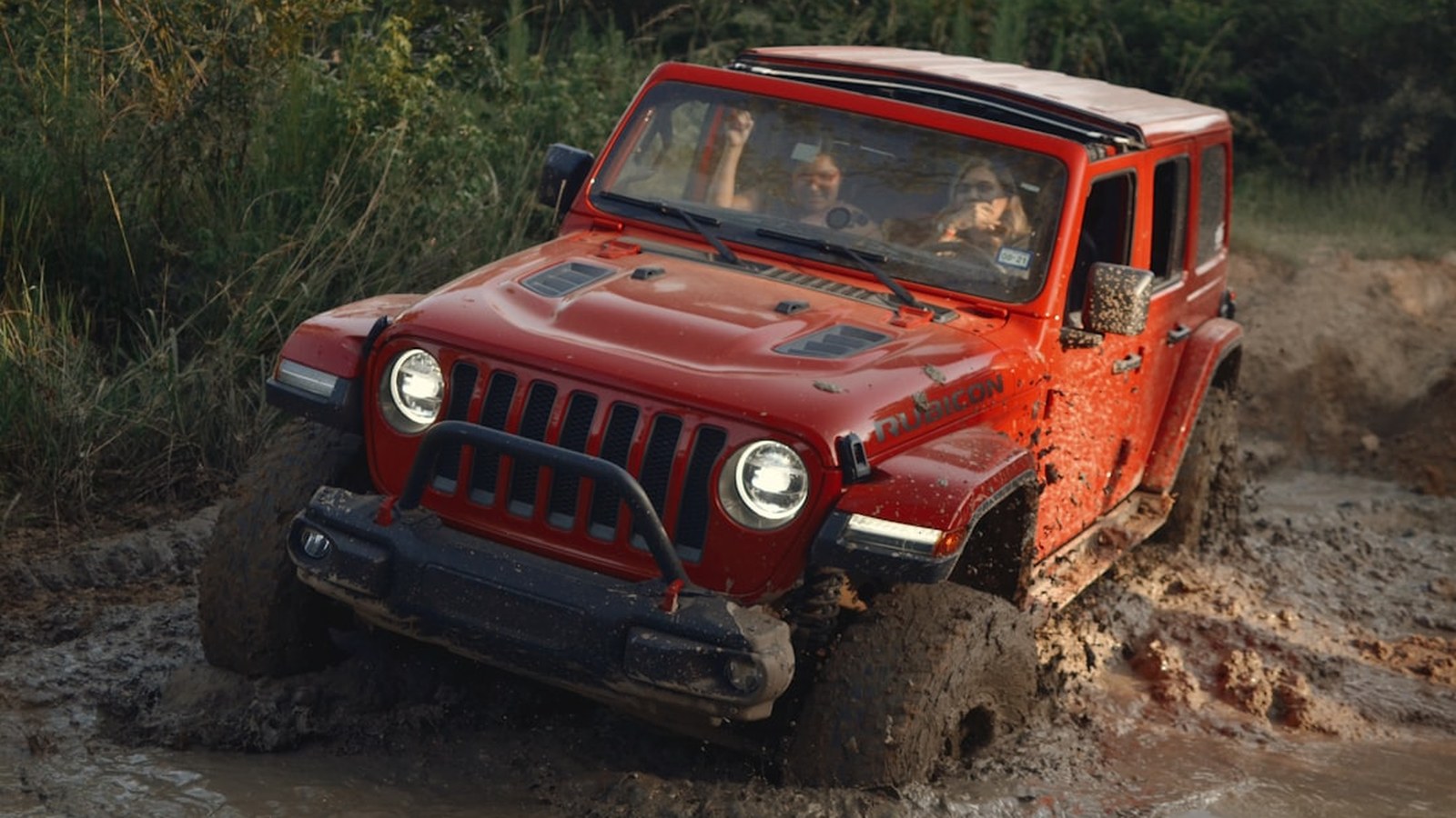 Red Jeep Wrangler Rubicon plowing through deep mud, spraying muck off its tires