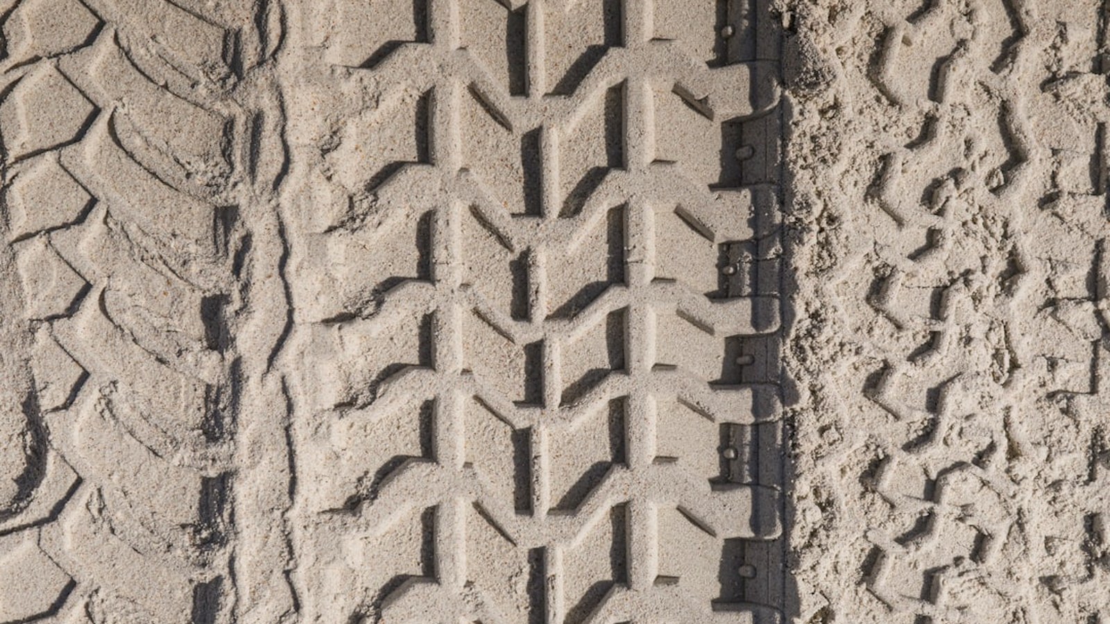Close-up of an aggressive off-road tire tread pressed into dirt, showing the deep lugs and gaps that define traction