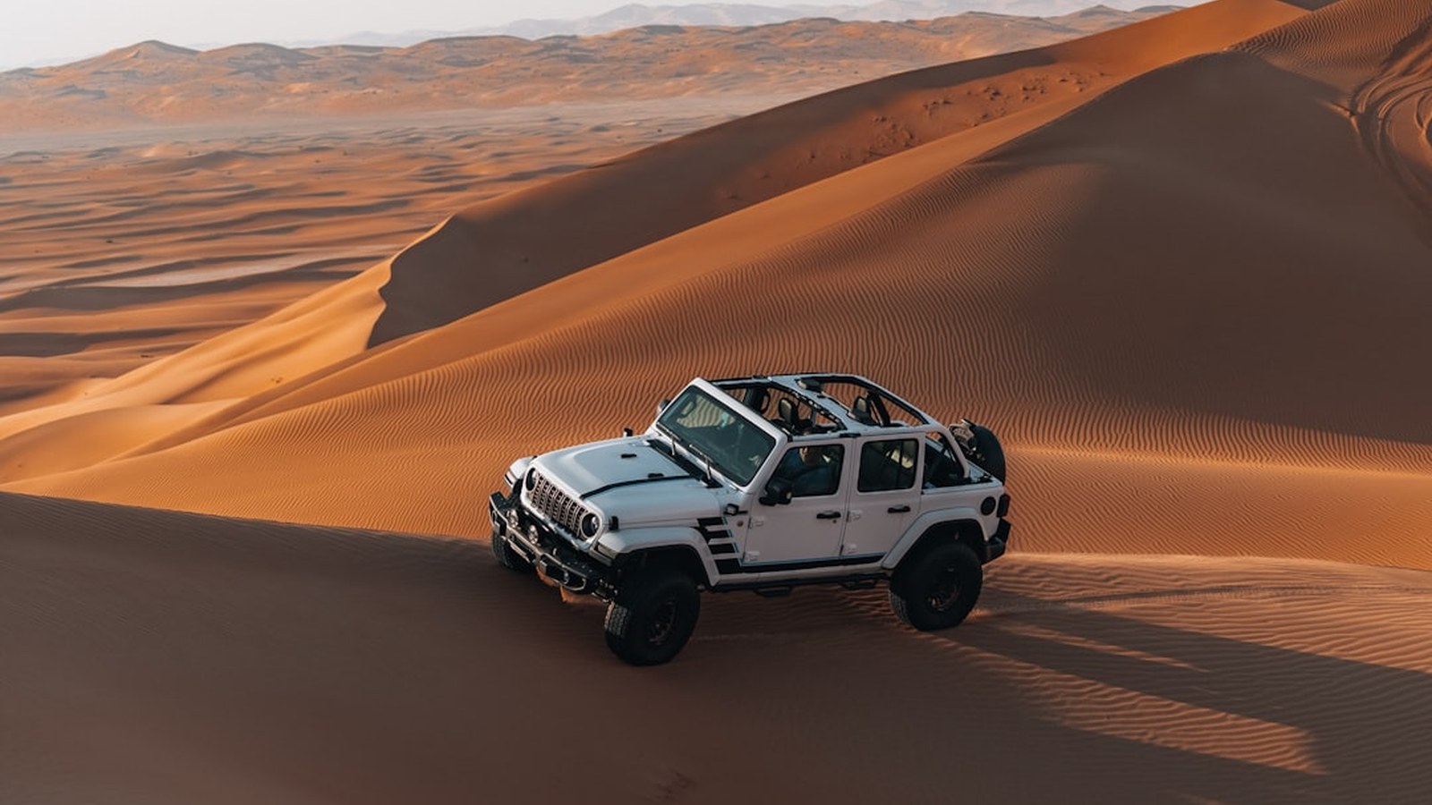 A white Jeep Wrangler working a golden desert dune slope at sunset