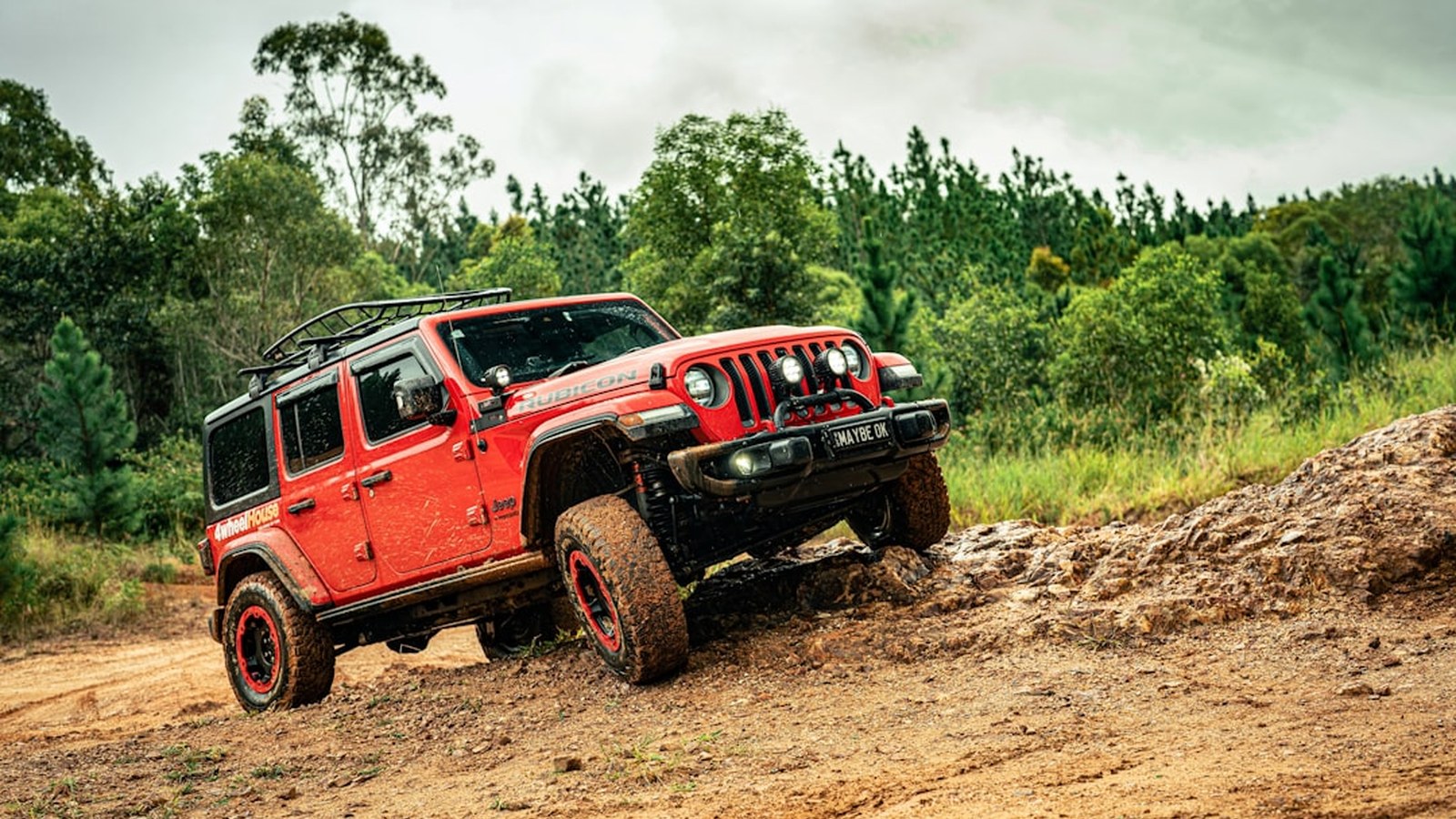 A red Jeep Rubicon articulating a front tire up a rock-and-dirt embankment