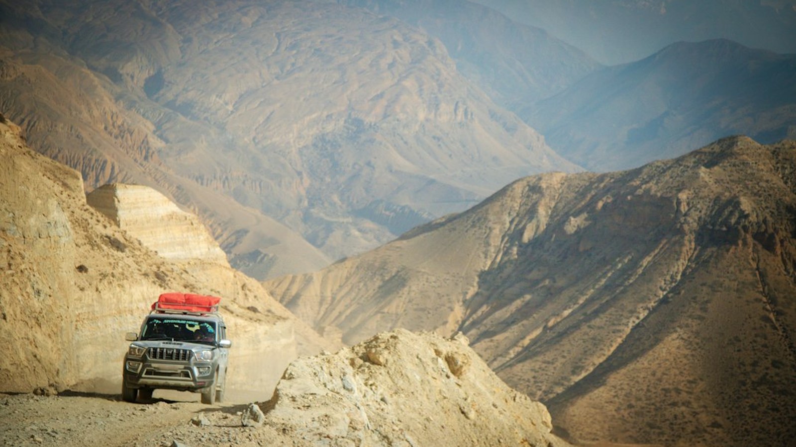 A lone 4x4 rig on a narrow dirt shelf road cutting through a vast remote canyon, far from any cell coverage