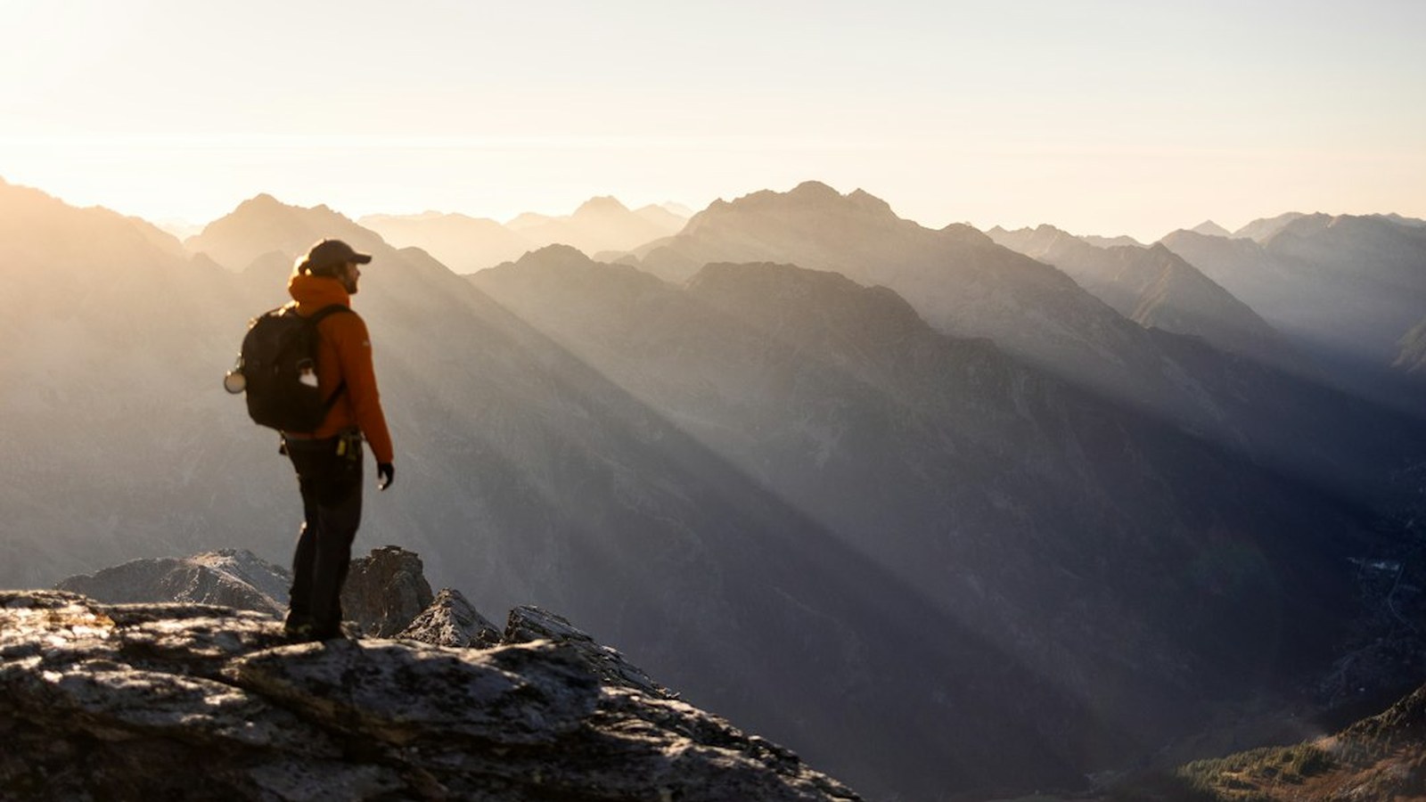 A solo backcountry traveler silhouetted on a high mountain ridge at sunrise, far from help