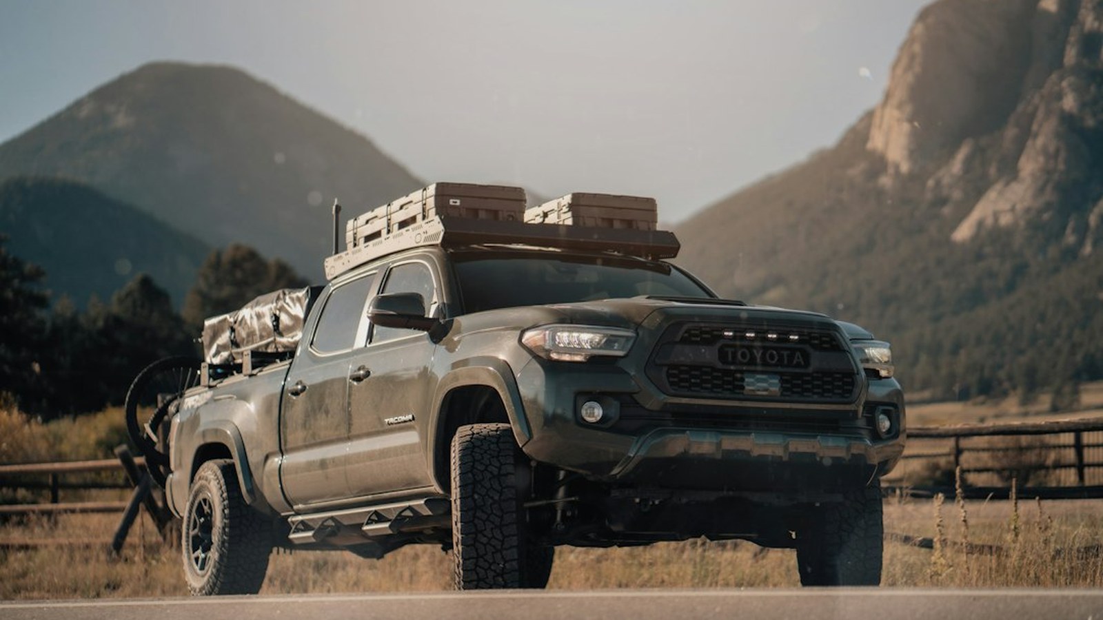 A single overland truck loaded with gear parked alone on a remote mountain road with rugged peaks behind