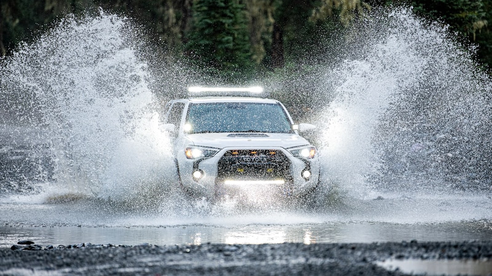 A Toyota 4Runner blasting through a deep river crossing with a dramatic water spray