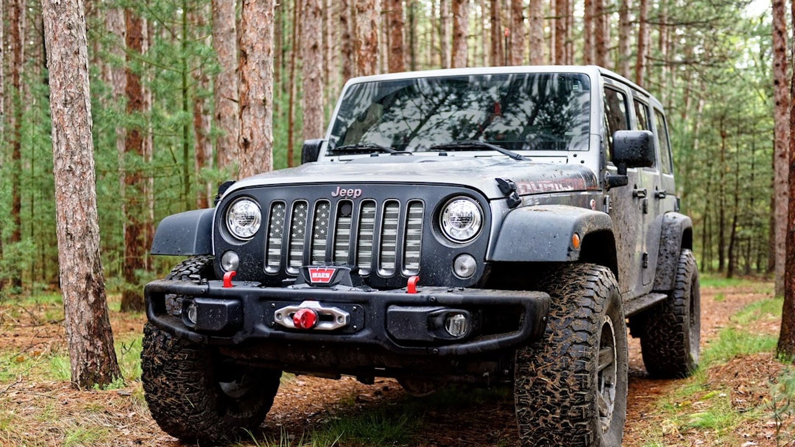 A Warn winch and hawse fairlead mounted in a heavy-duty steel front bumper on a muddy Jeep Wrangler