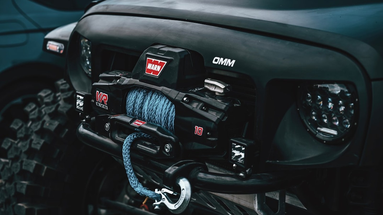 A Warn winch with blue synthetic rope spooled on the drum mounted on an off-road bumper