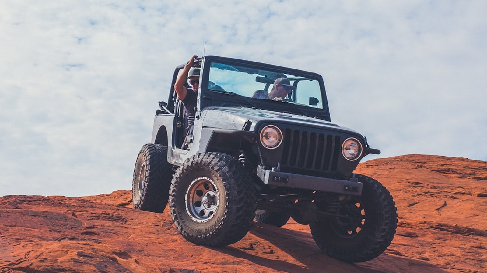 A Jeep climbing a steep red-rock slickrock obstacle on a desert trail