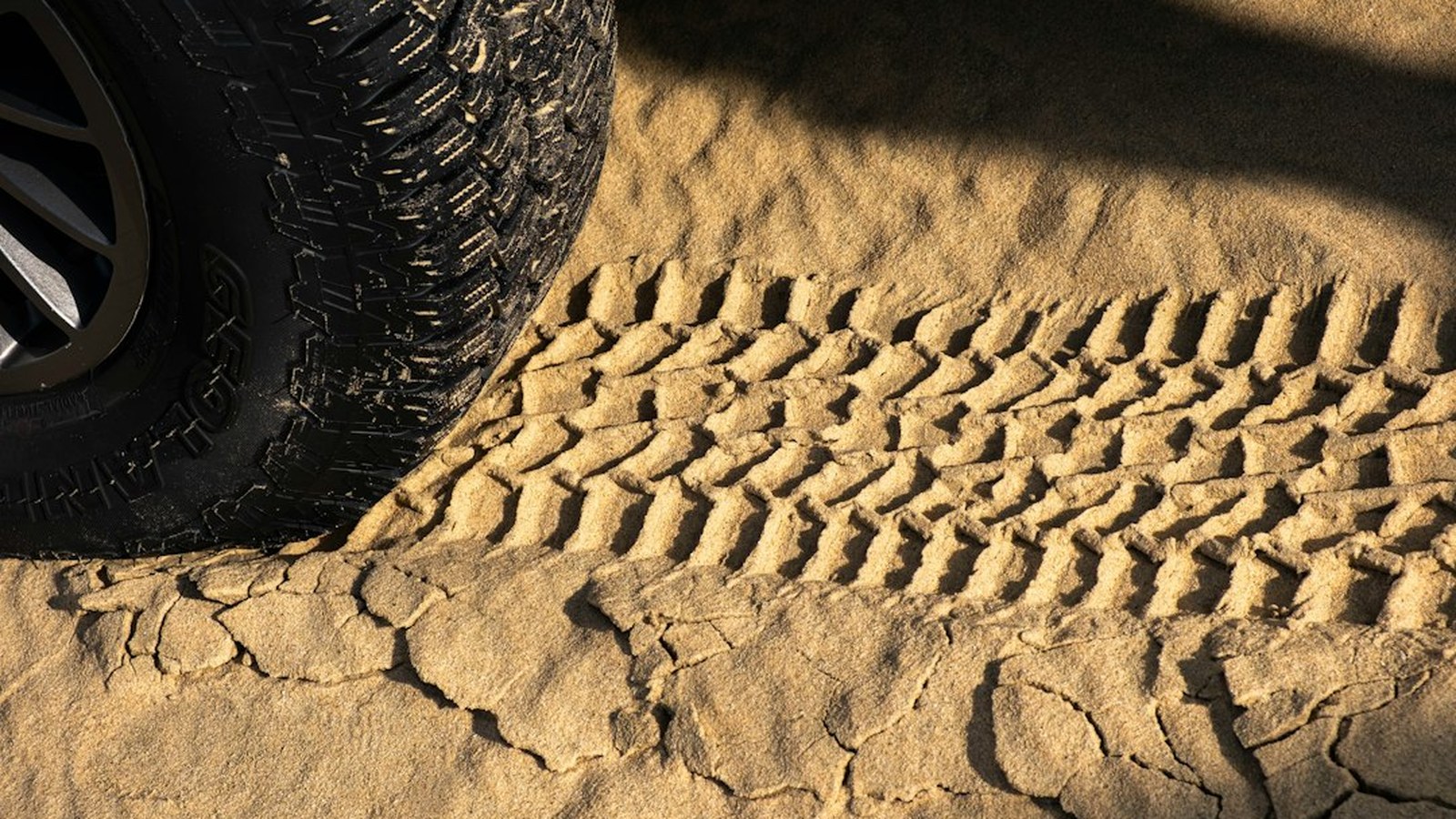 Close-up of an all-terrain off-road tire on sandy desert ground with a fresh track