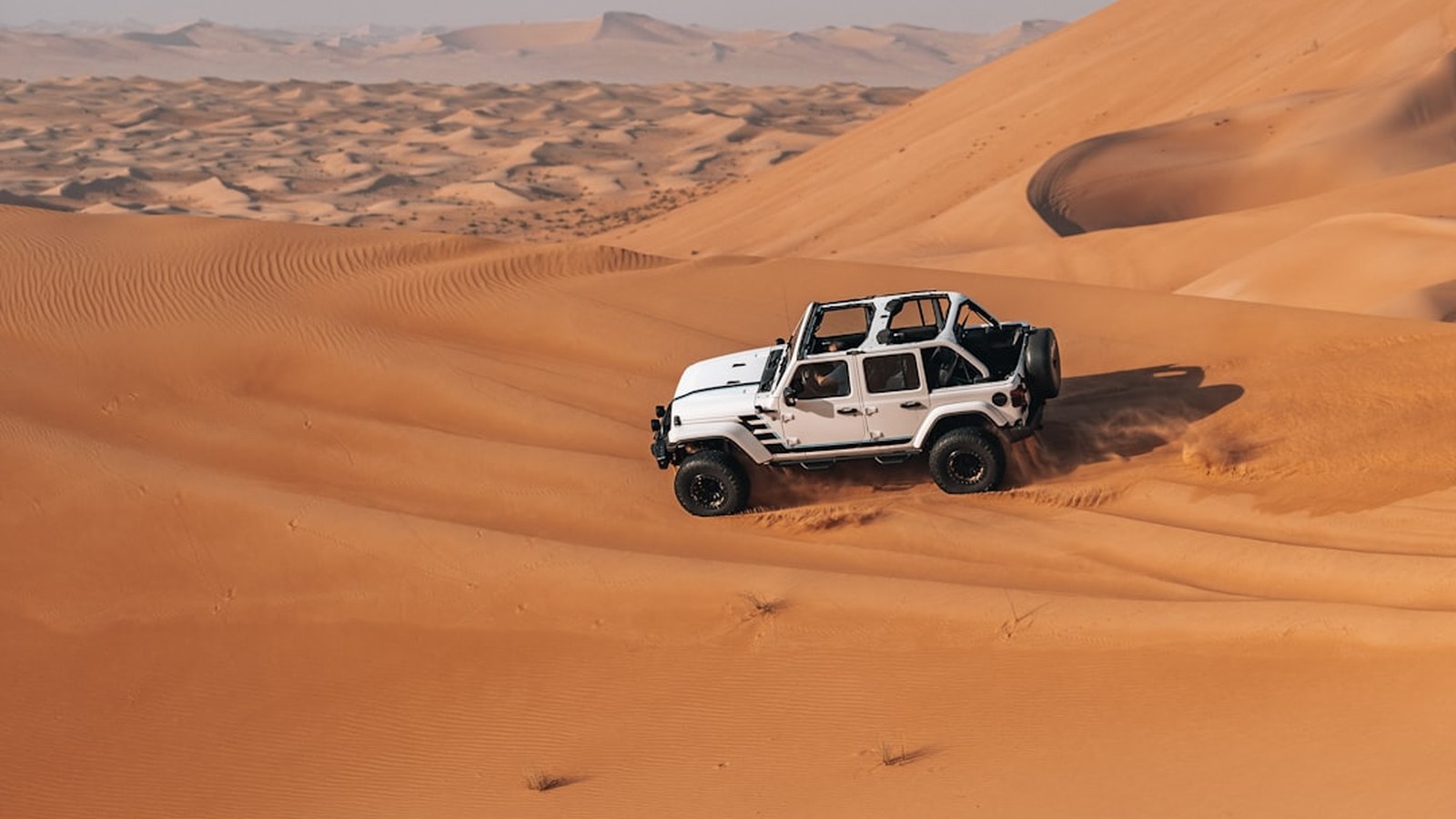 White Jeep climbing a steep sand dune under a clear sky