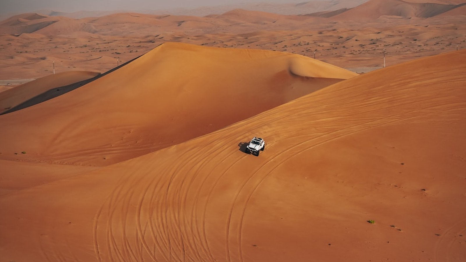 White 4x4 driving down a large red sand dune leaving tracks behind it