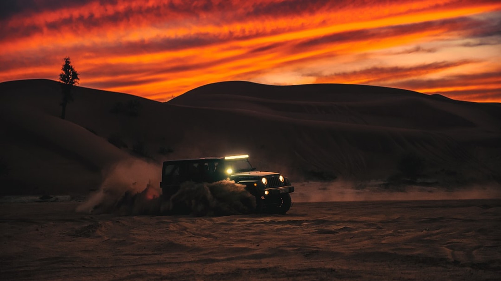 Jeep 4x4 plowing through soft sand and throwing up a spray at sunset