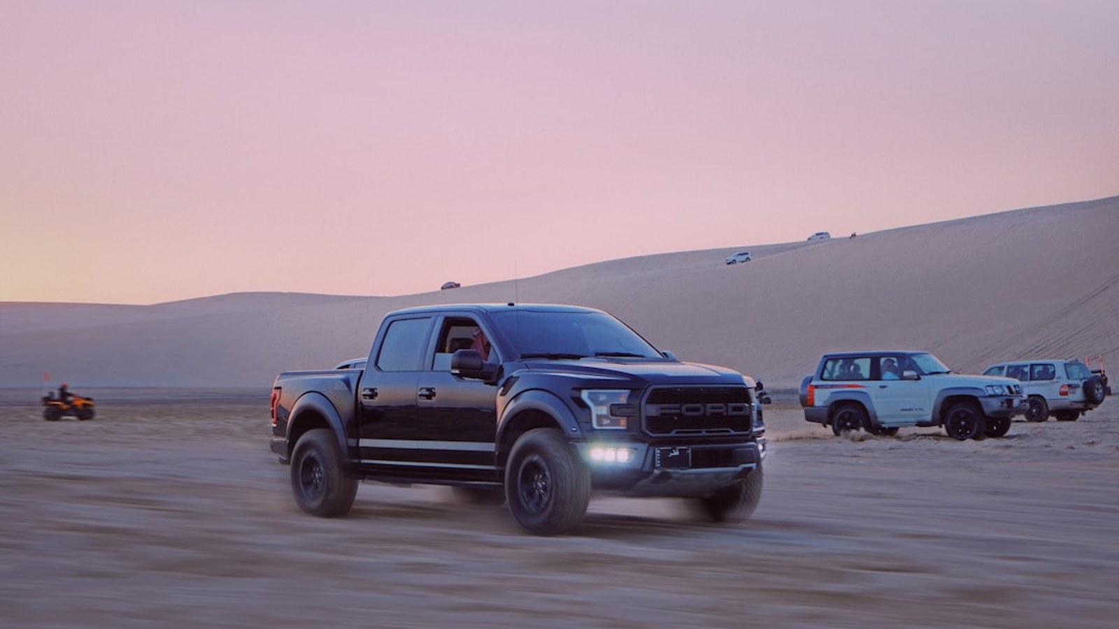 4x4 trucks driving across desert sand at golden hour with a pink sky