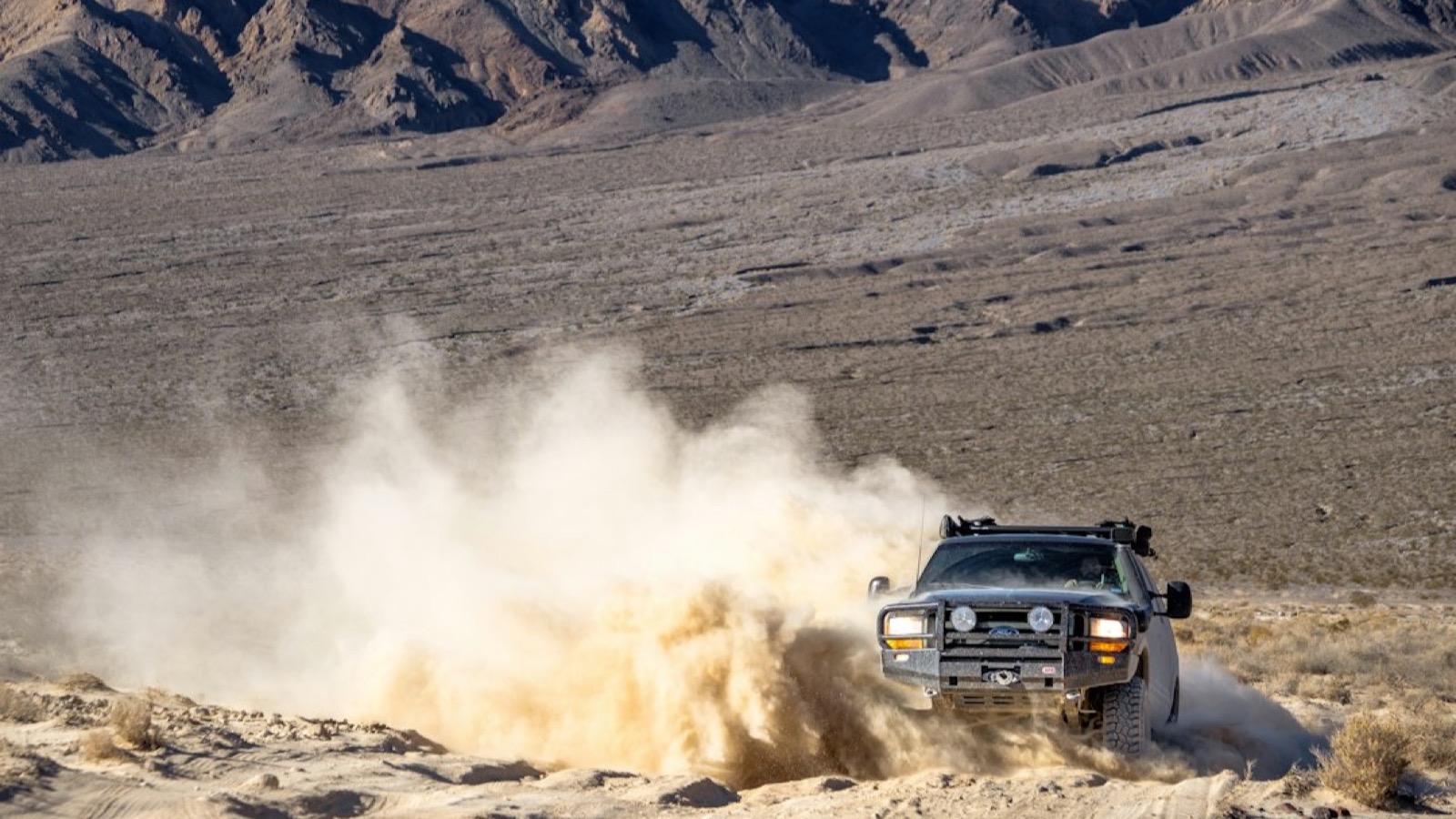 Classic 4x4 pickup with an ARB bumper blasting a large dust plume along a desert trail