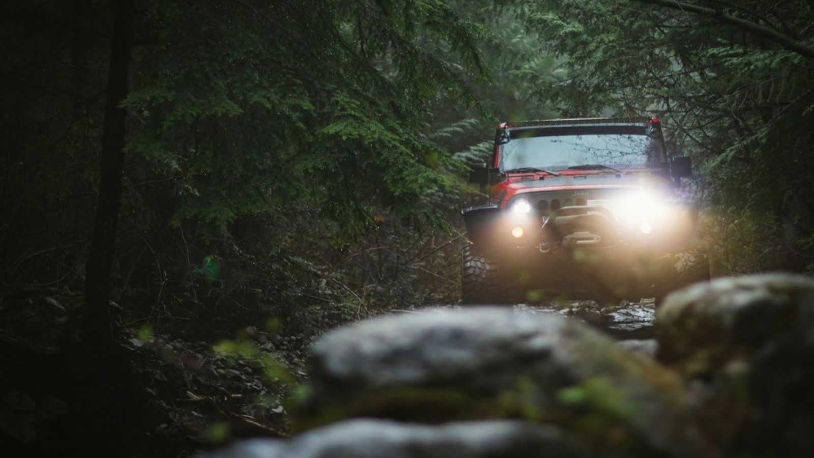 Jeep Wrangler Rubicon articulating over a rock ledge with its front wheel flexed upward on a trail