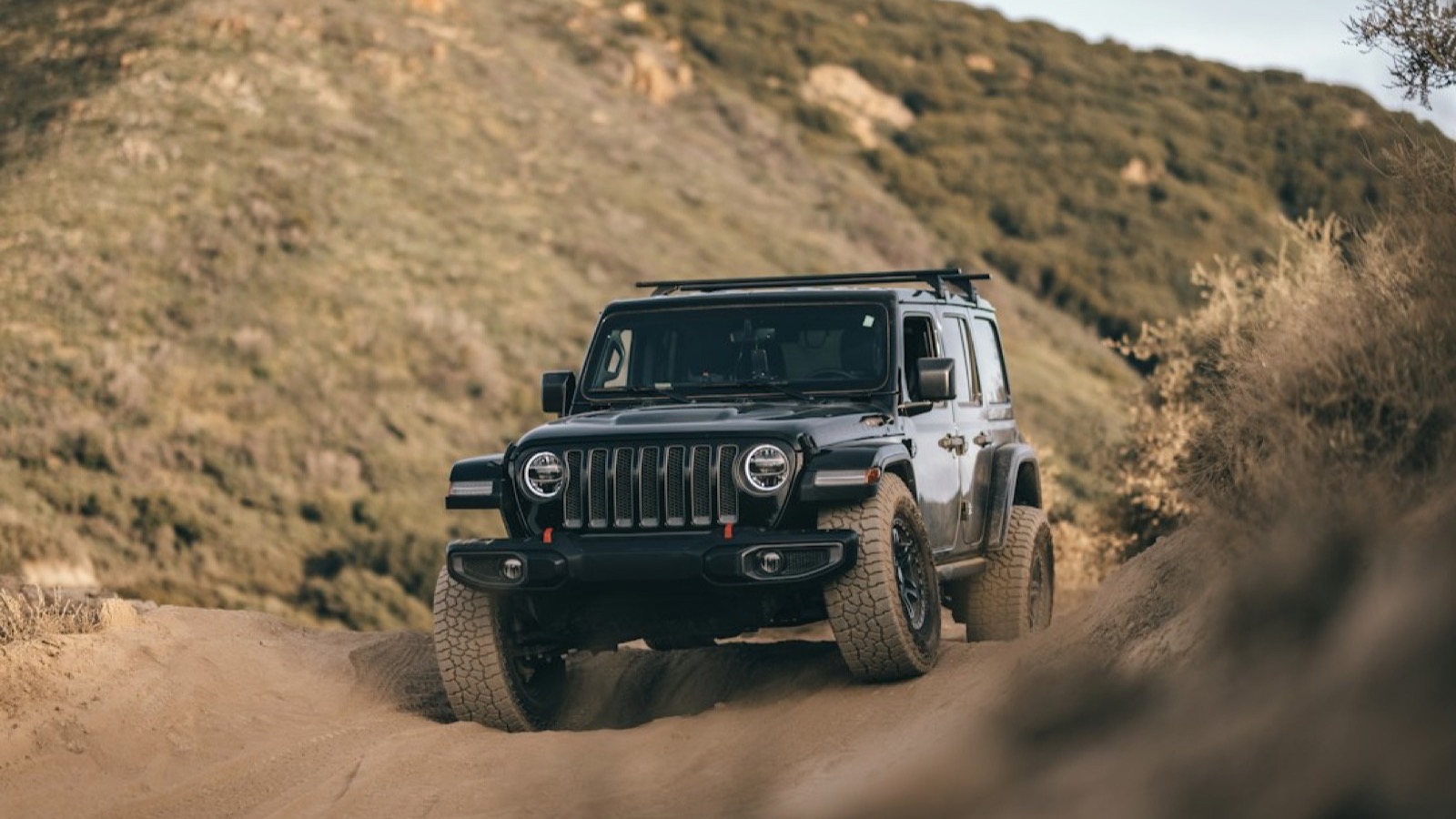 Black Jeep Wrangler Rubicon climbing a rutted sandy trail with tires biting loose terrain