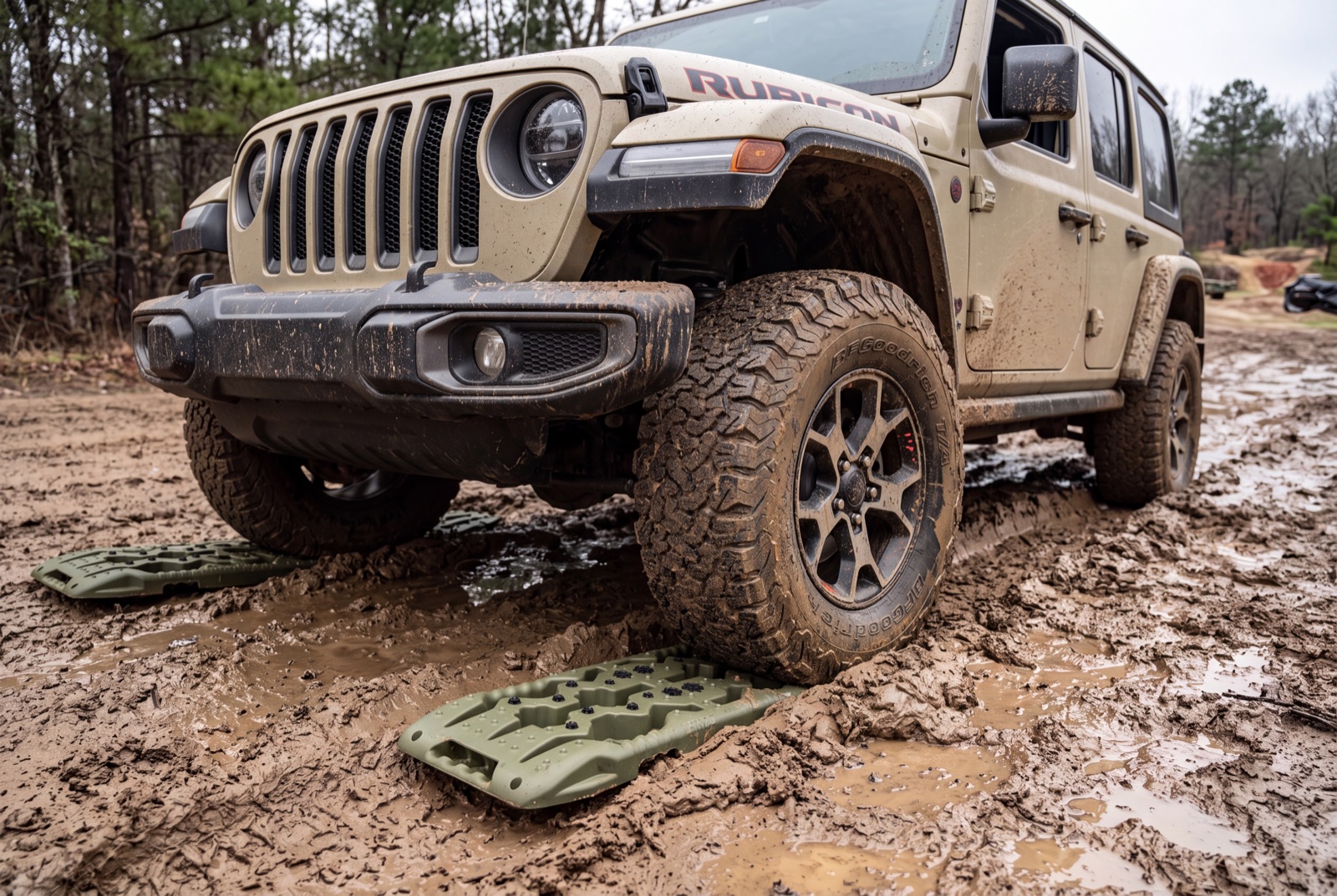 A Jeep Wrangler Rubicon climbing onto traction boards laid in deep mud