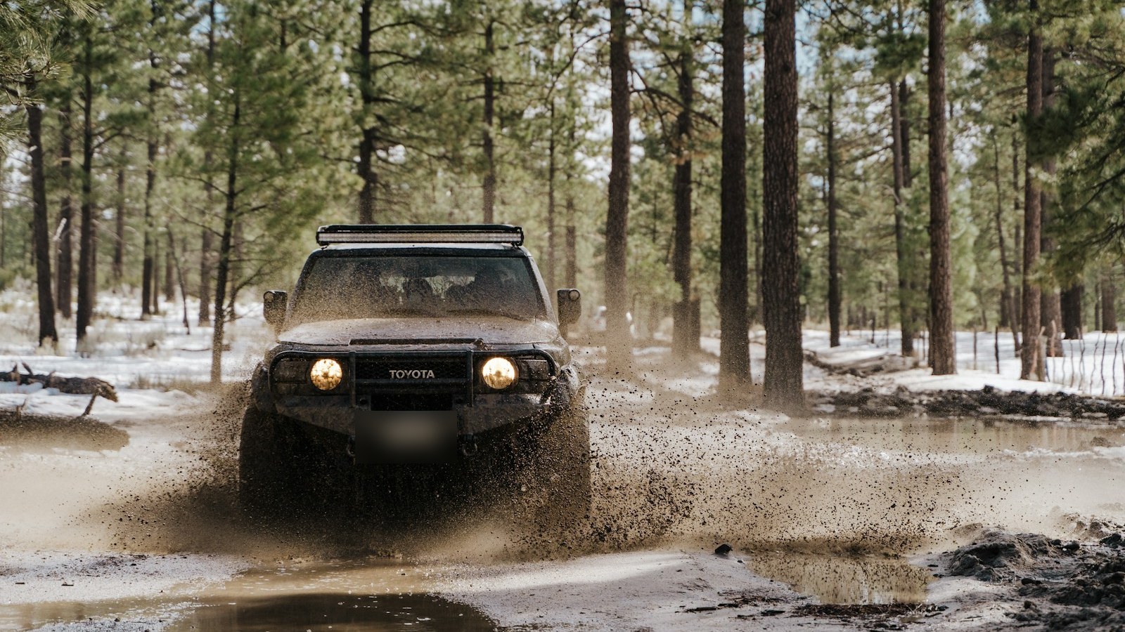 A 4x4 blasting through a muddy puddle on a forest trail, spraying mud