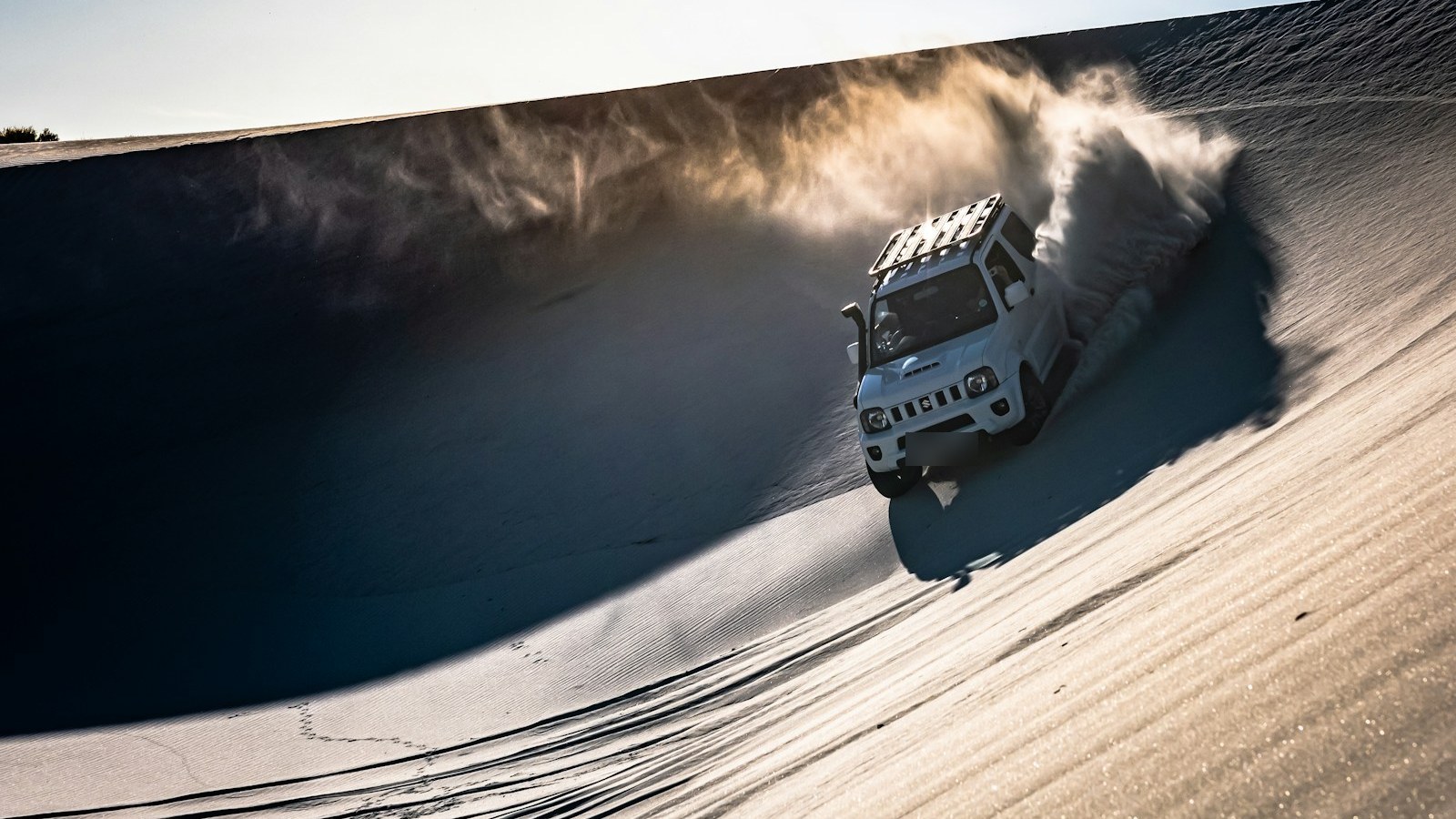 A compact 4x4 carving through desert sand dunes throwing up a plume of sand