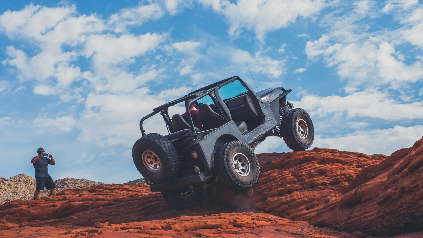 A grey 4x4 climbing up a steep section of red rock on a technical trail