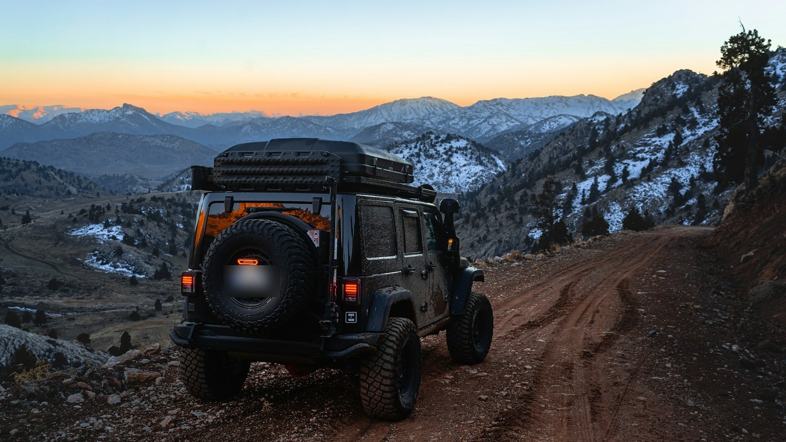 A Jeep parked on a dirt mountain trail with a wide view of the terrain ahead