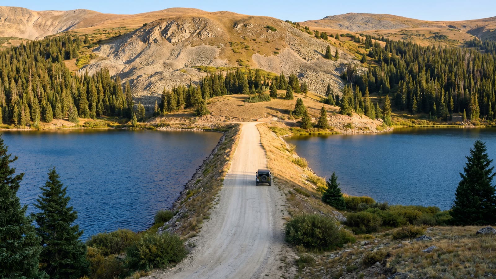 A 4x4 rig on the rocky road crossing between the two Chinns Lake reservoirs in the Colorado high country at golden hour