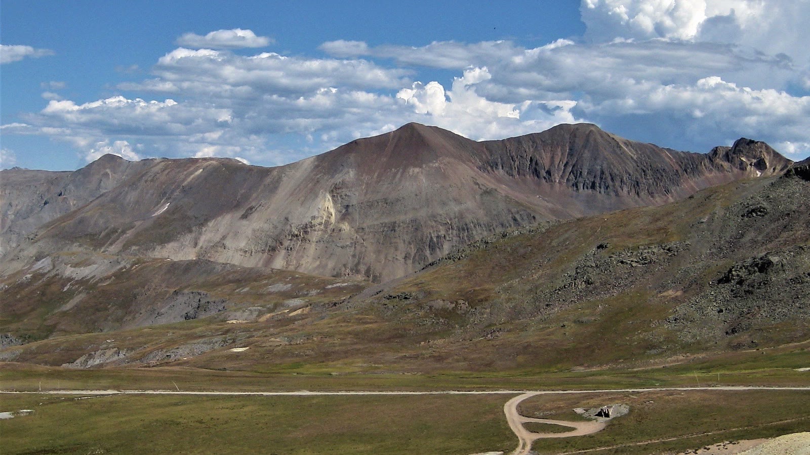 A rocky alpine 4x4 road climbing above treeline toward a bare tundra ridge under a big Colorado sky
