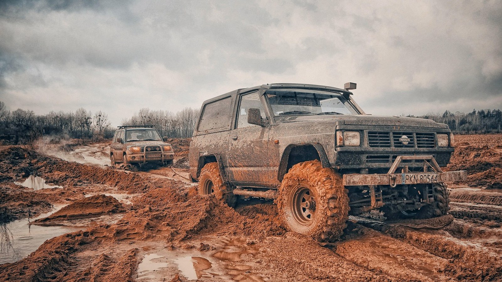 A mud-caked 4x4 hooked to a recovery strap on a churned-up trail