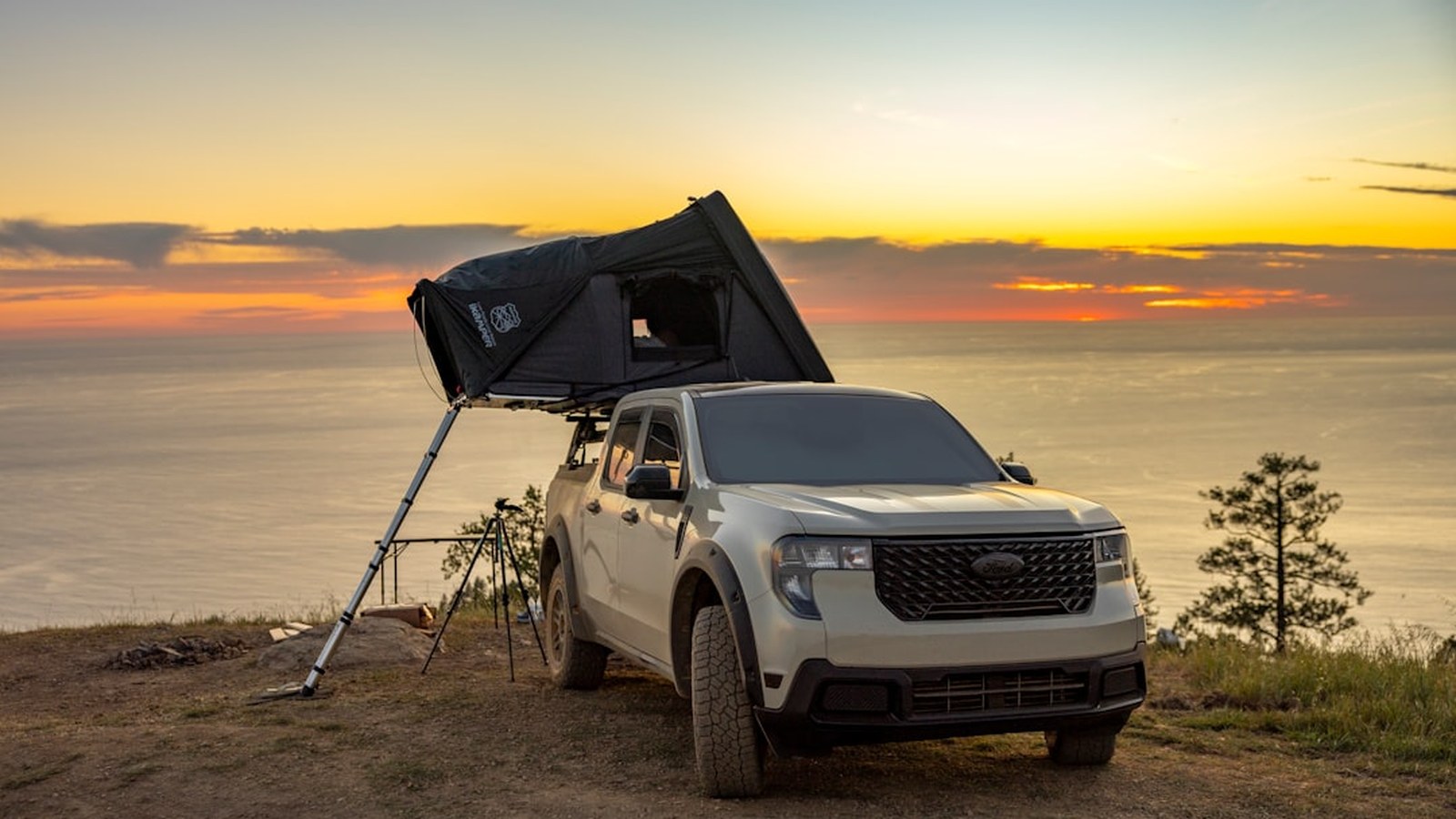 Overland truck with a rooftop tent set up at a remote camp in golden light