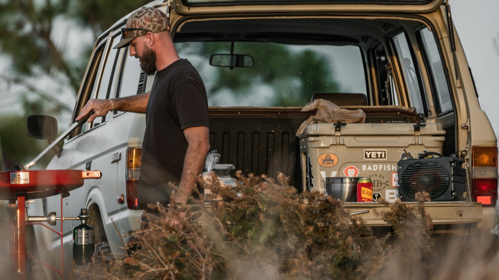 Overlander at the open rear of a 4x4 truck loaded with camp and storage gear