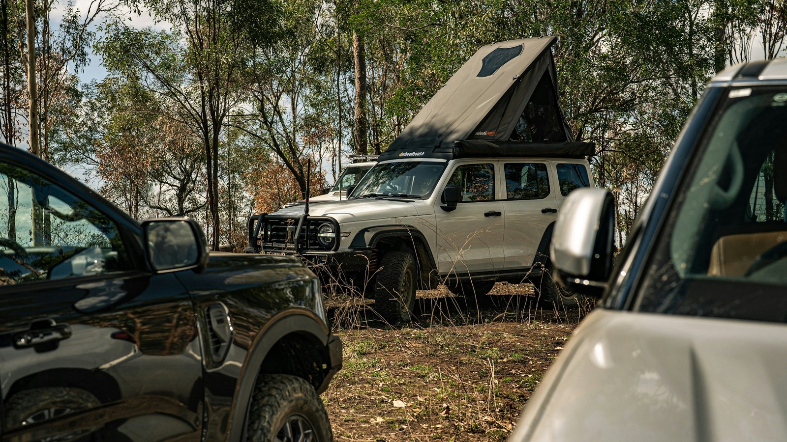 Two off-road 4x4 rigs with a rooftop tent set up at a wooded overland camp