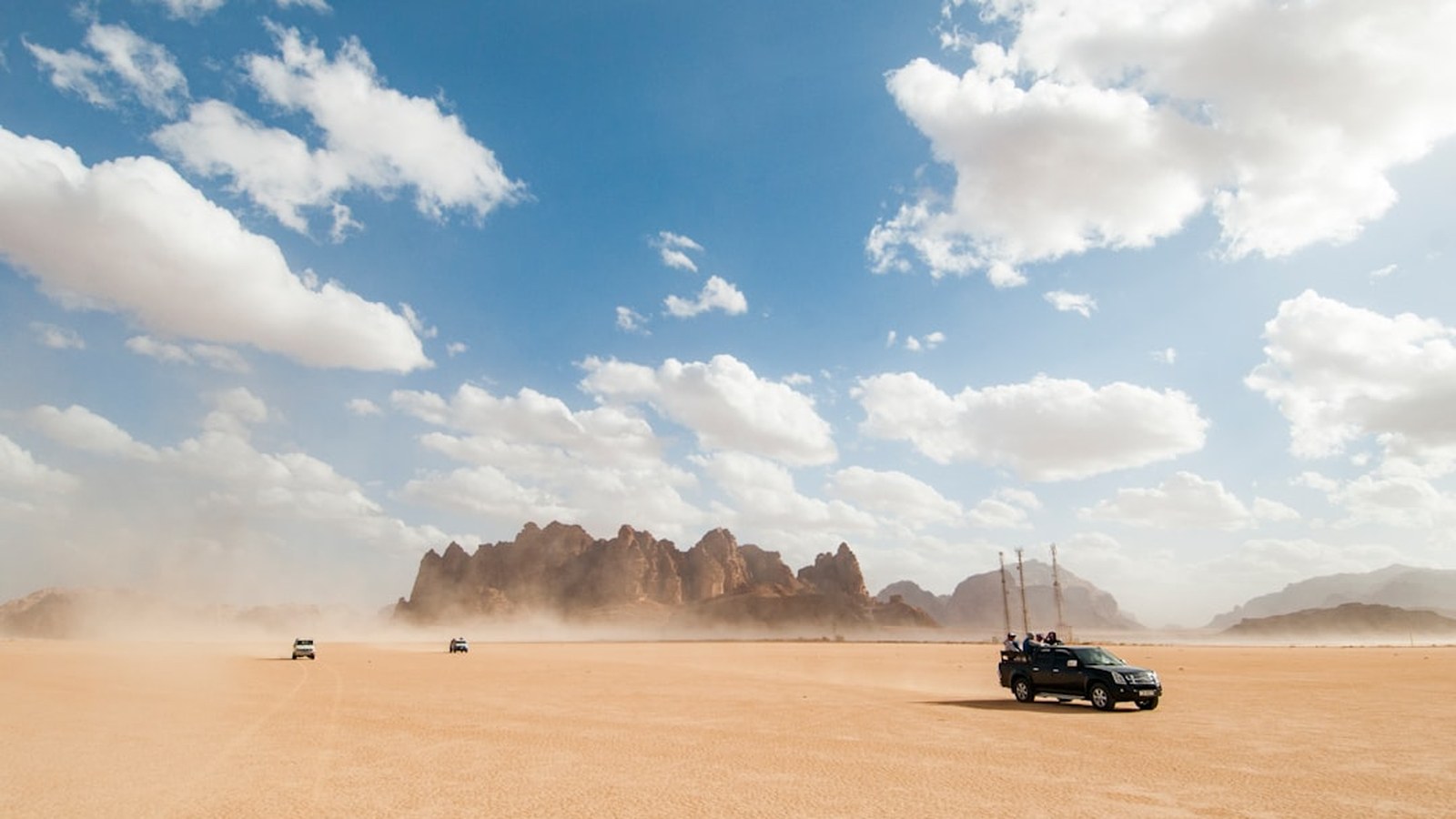 A group of 4x4 rigs traveling together across open desert, kicking up dust