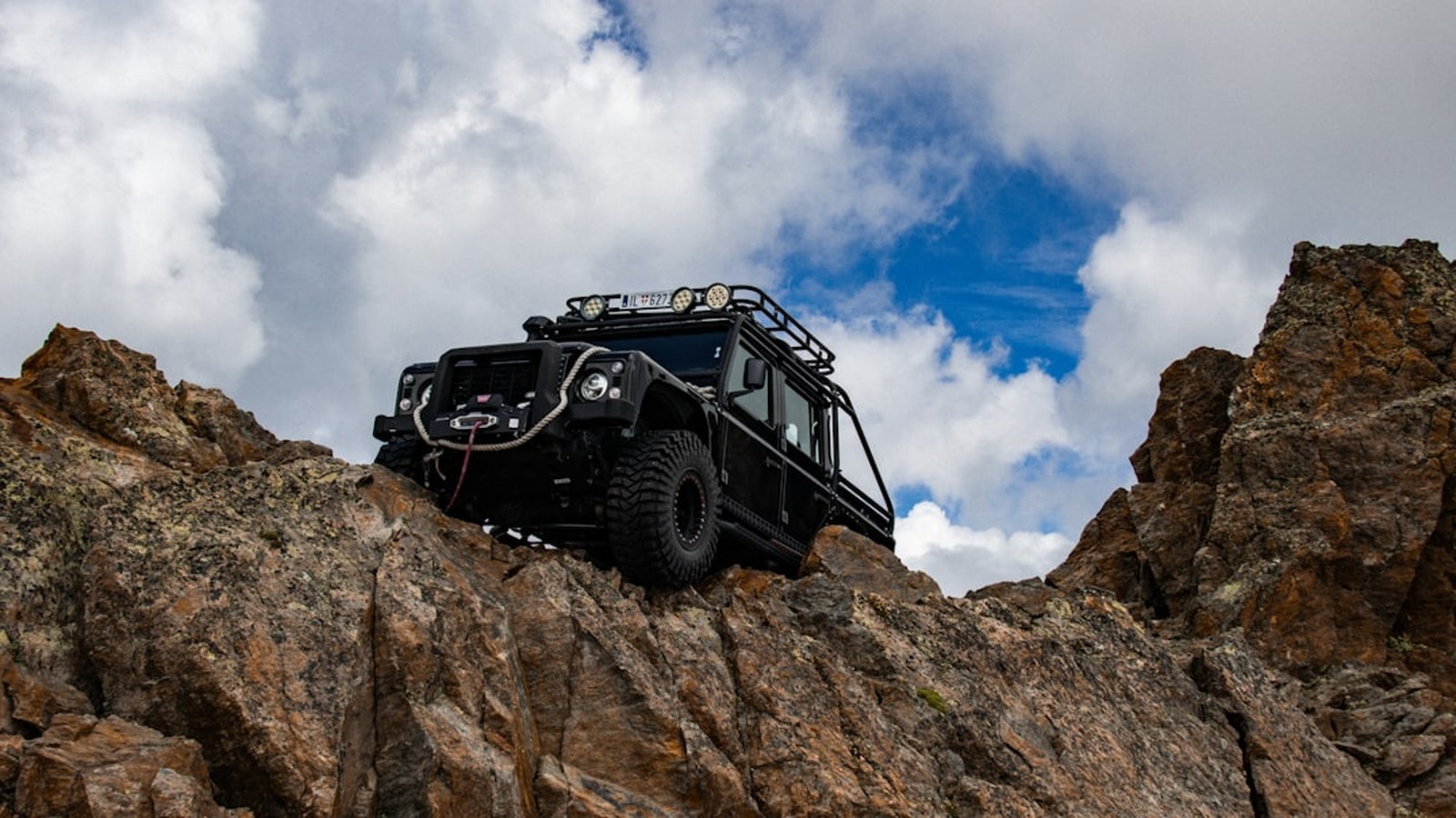 A kitted-out 4x4 rig perched on rocky mountain terrain under a dramatic sky
