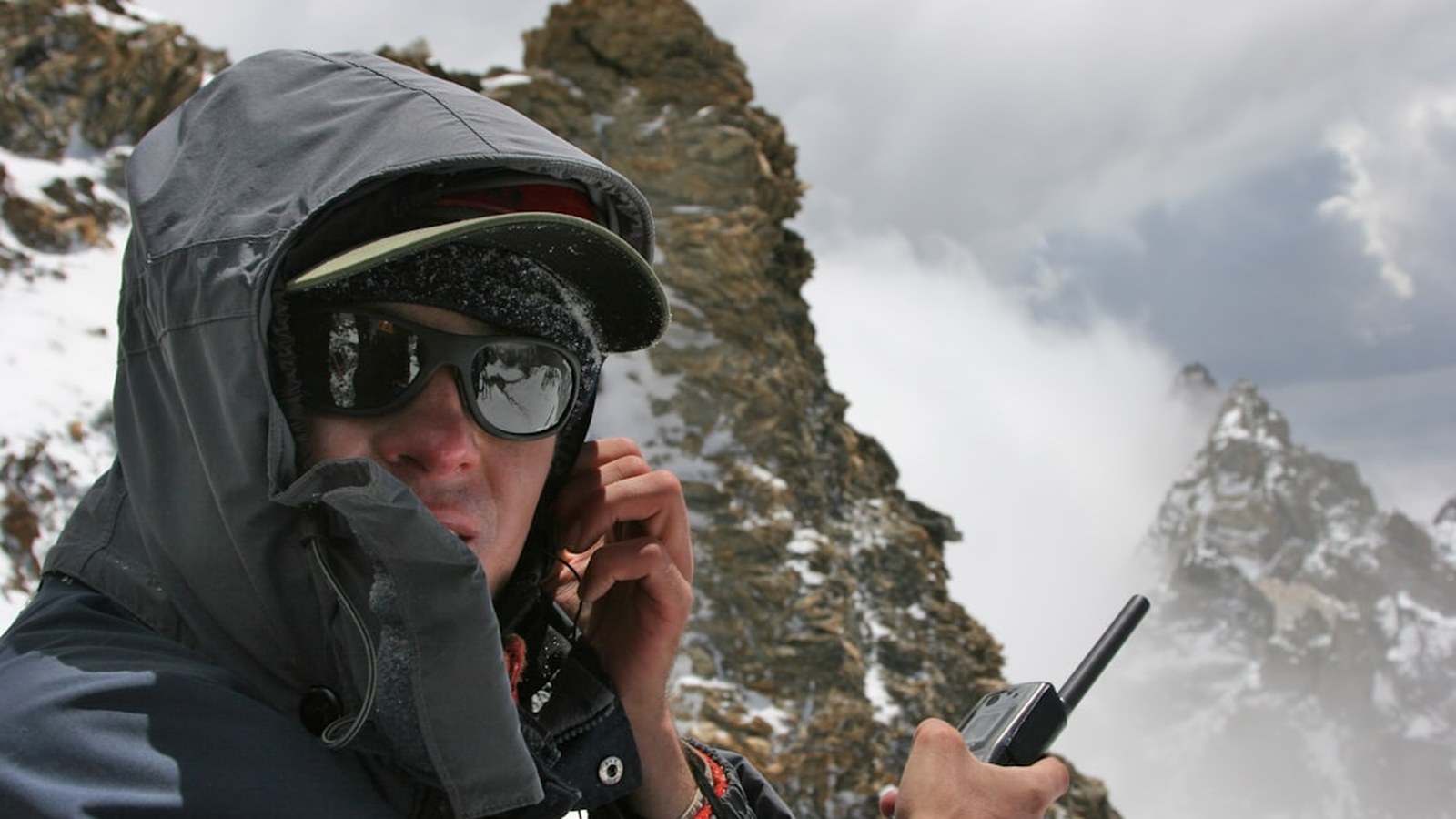 A person on a snowy mountain ridge holding a handheld two-way radio