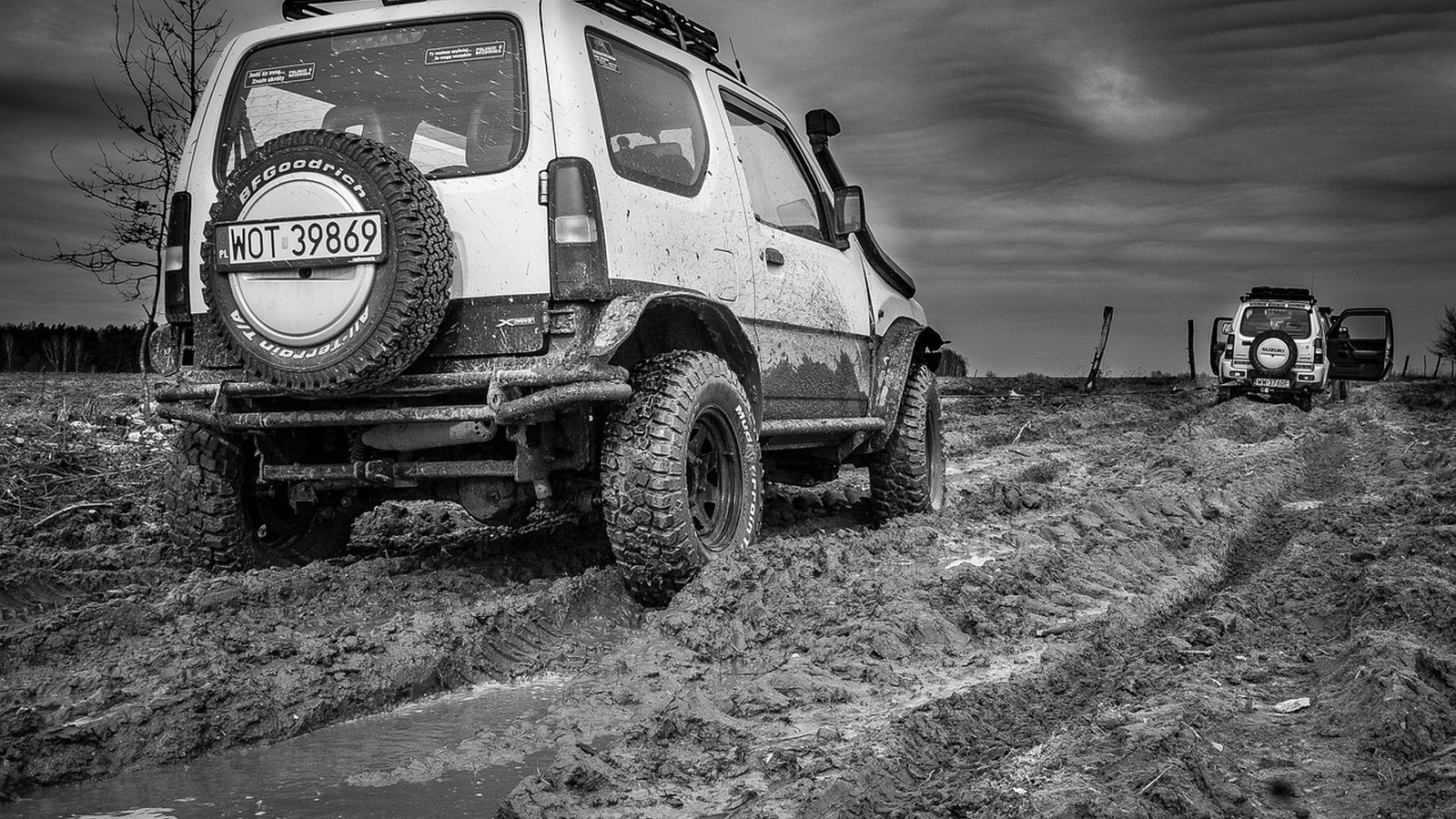 A mud-caked compact 4x4 with aggressive mud-terrain tires and a spare, showing hard trail use.