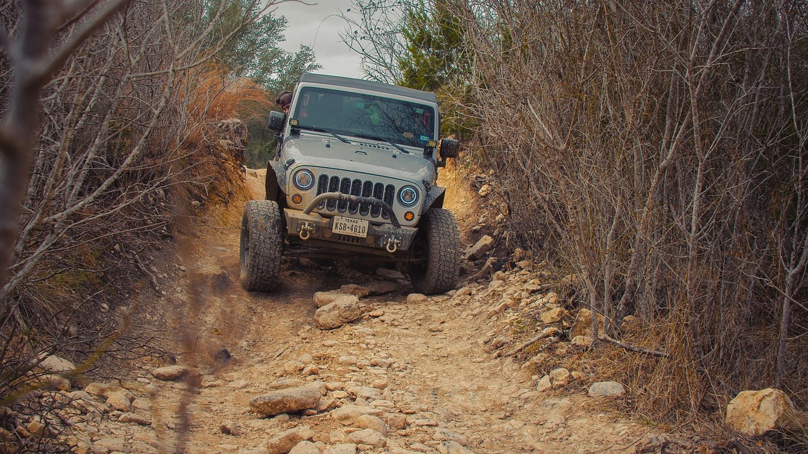 A lone 4x4 descends a rocky, rutted trail through brush, the kind of obstacle a solo overlander has to weigh carefully.